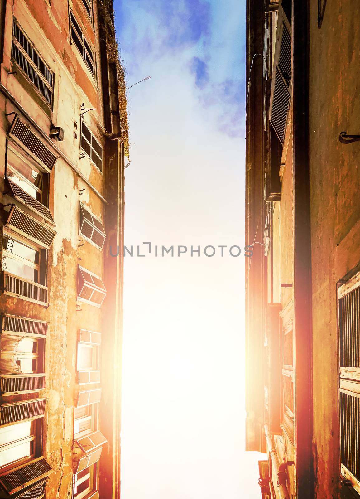 illuminated cloudy sky of the sun seen through the ancient buildings of an alley in Rome during the day. Bottom view with upward perspective.