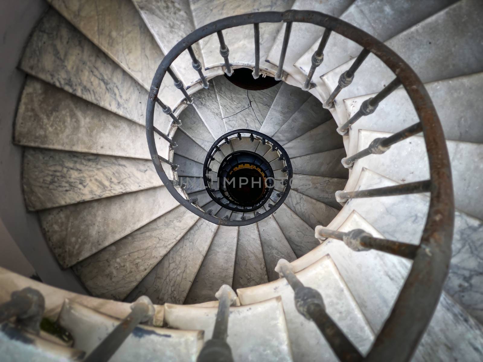 Ancient spiral staircase with decorated wrought iron handrails and marble steps inside an old palace in Rome. Top to bottom view with a perspective effect