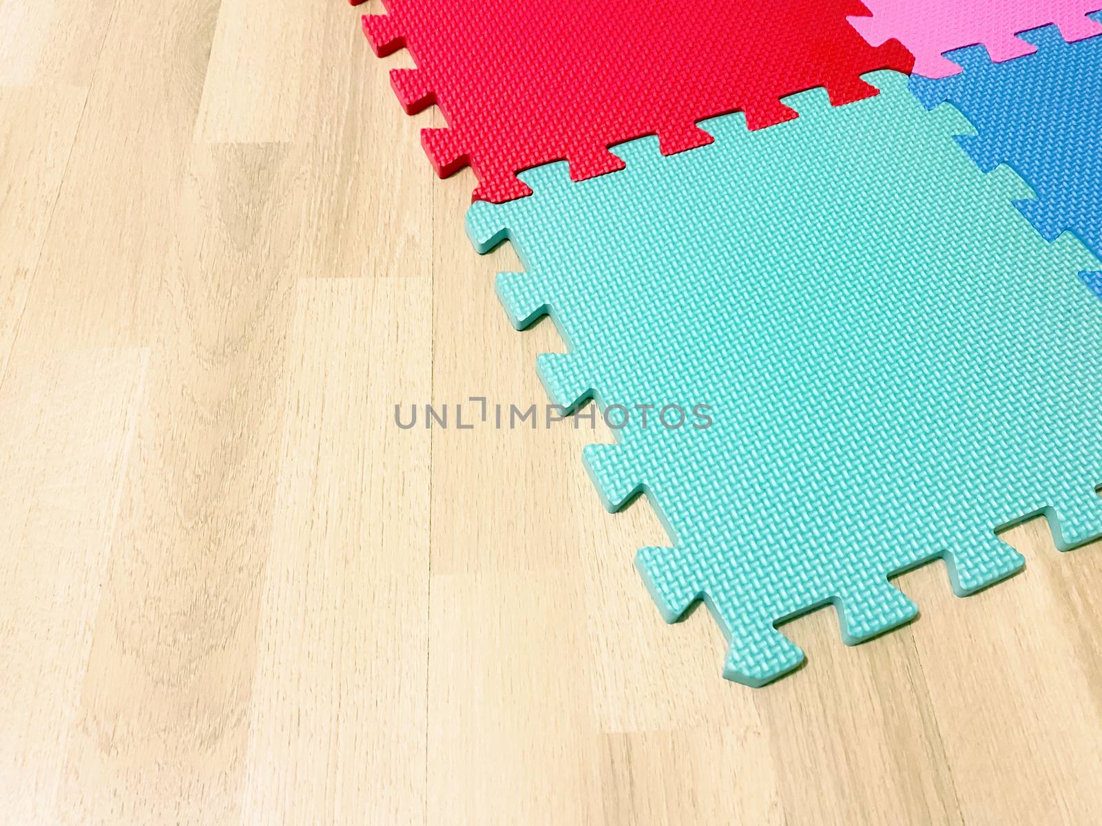 Soft rubber mat composed of colored blocks intersected with each other on a wooden floor. Suitable for children to play or for yoga exercises. Interior shot