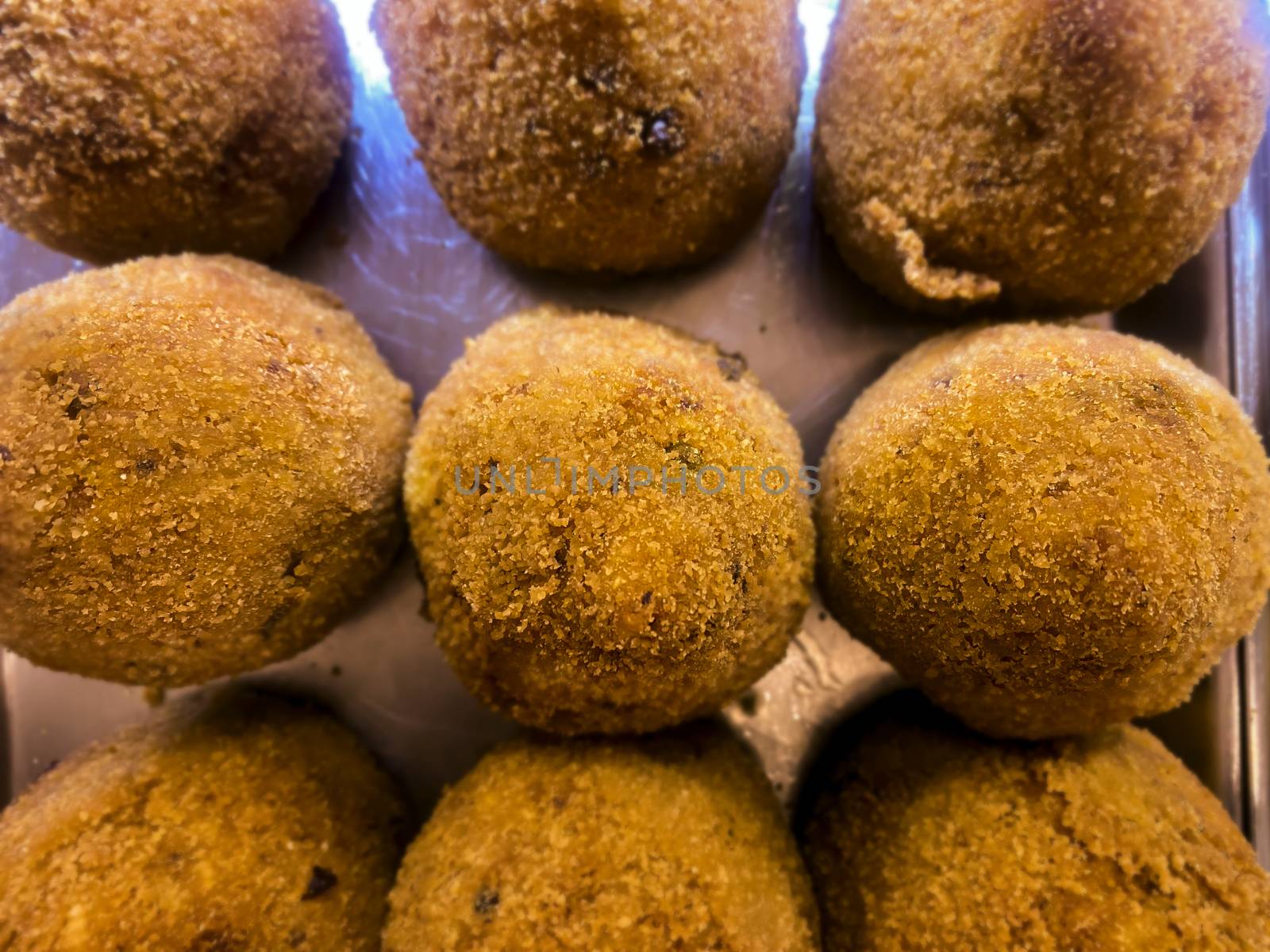 Sicilian arancini arranged on a metal tray and displayed for sale. Typical Sicilian recipe. Famous Italian food. Italian street food