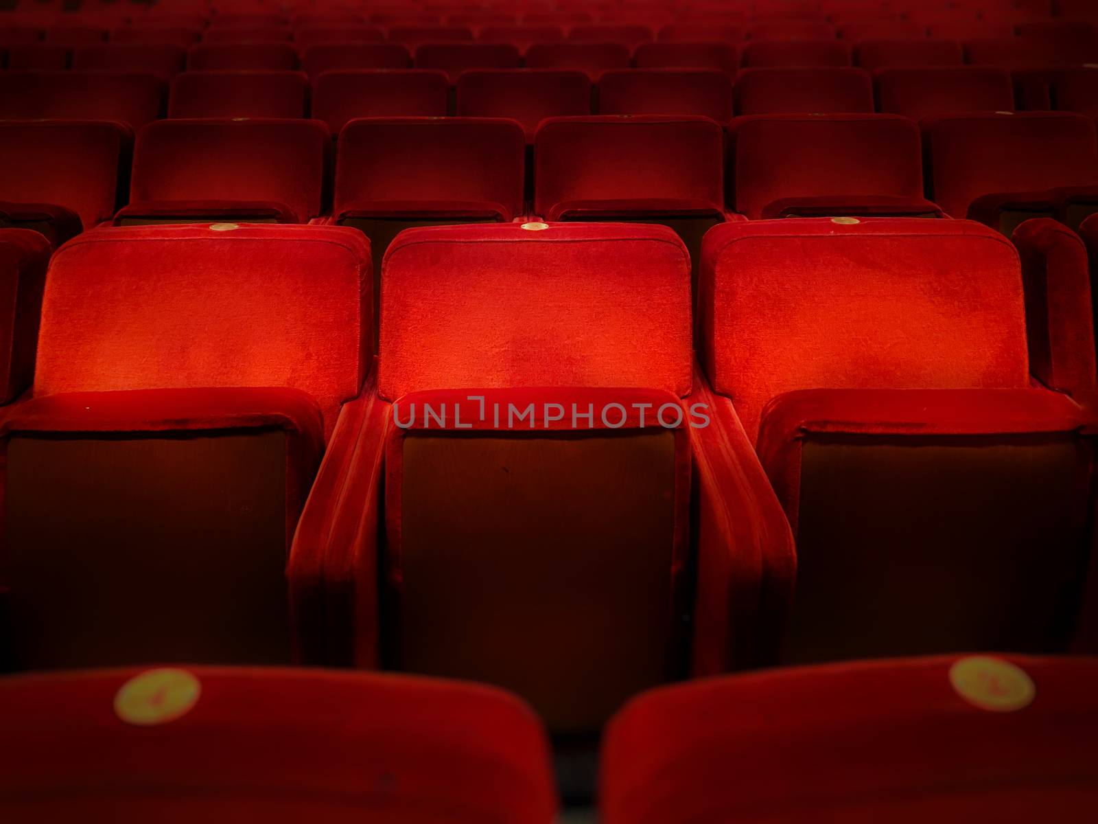 Three empty red velvet armchairs illuminated inside a concert hall