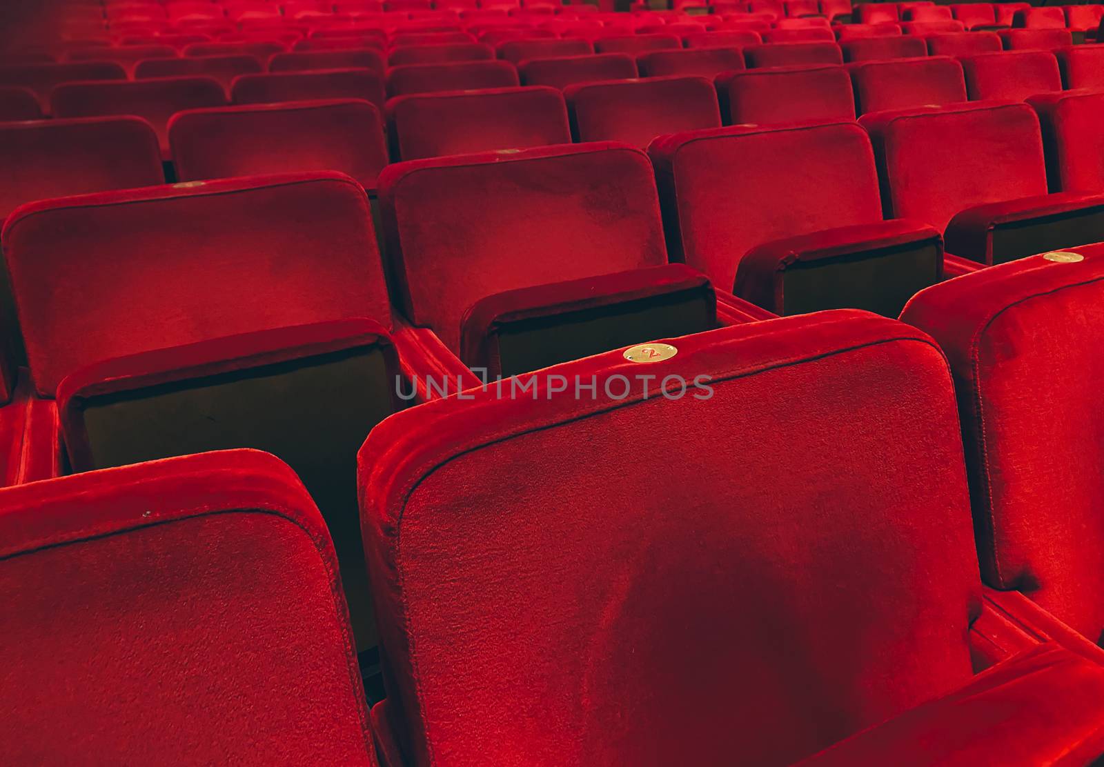 Empty red velvet armchairs illuminated inside a concert hall