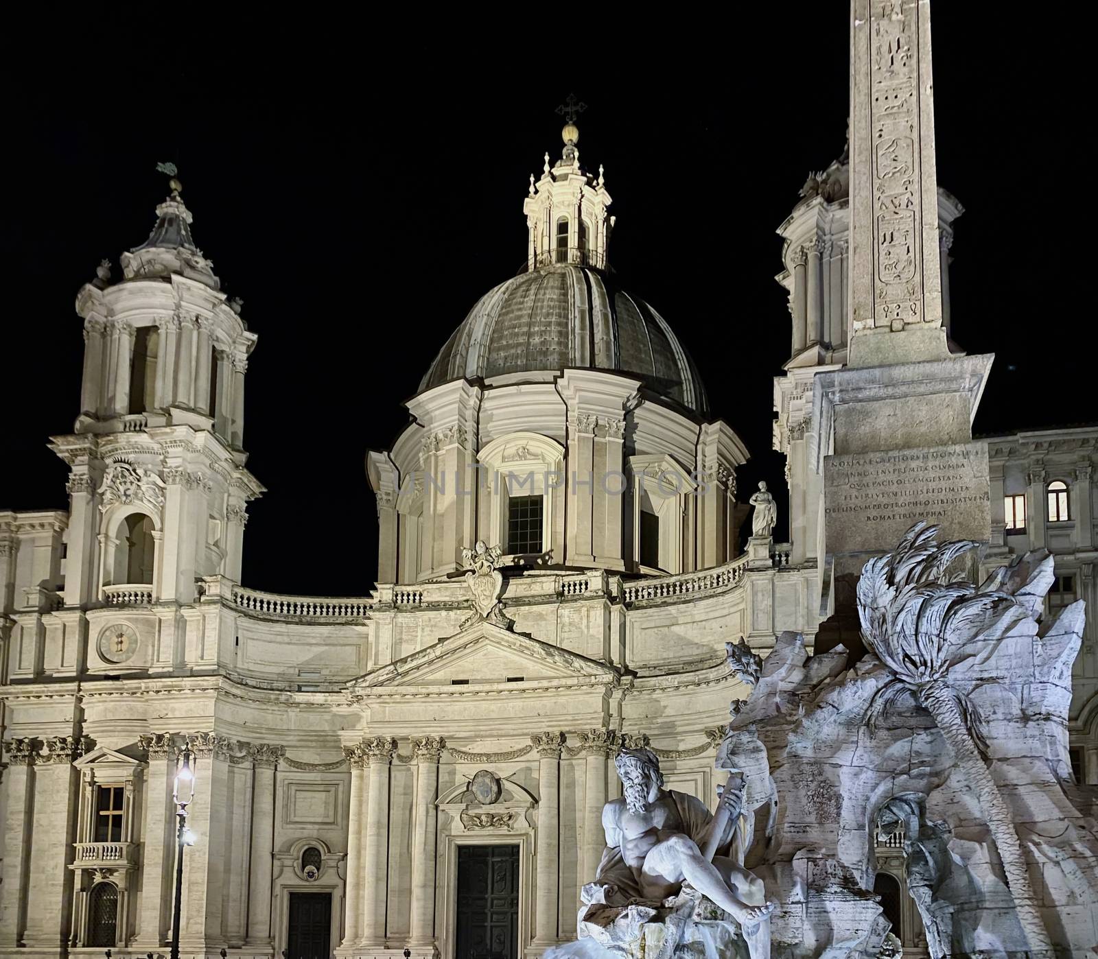 Night shot of the illuminated facade of the baroque church of Sant'Agnese in Agone with the fountain of the four rivers in Piazza Navona in Rome