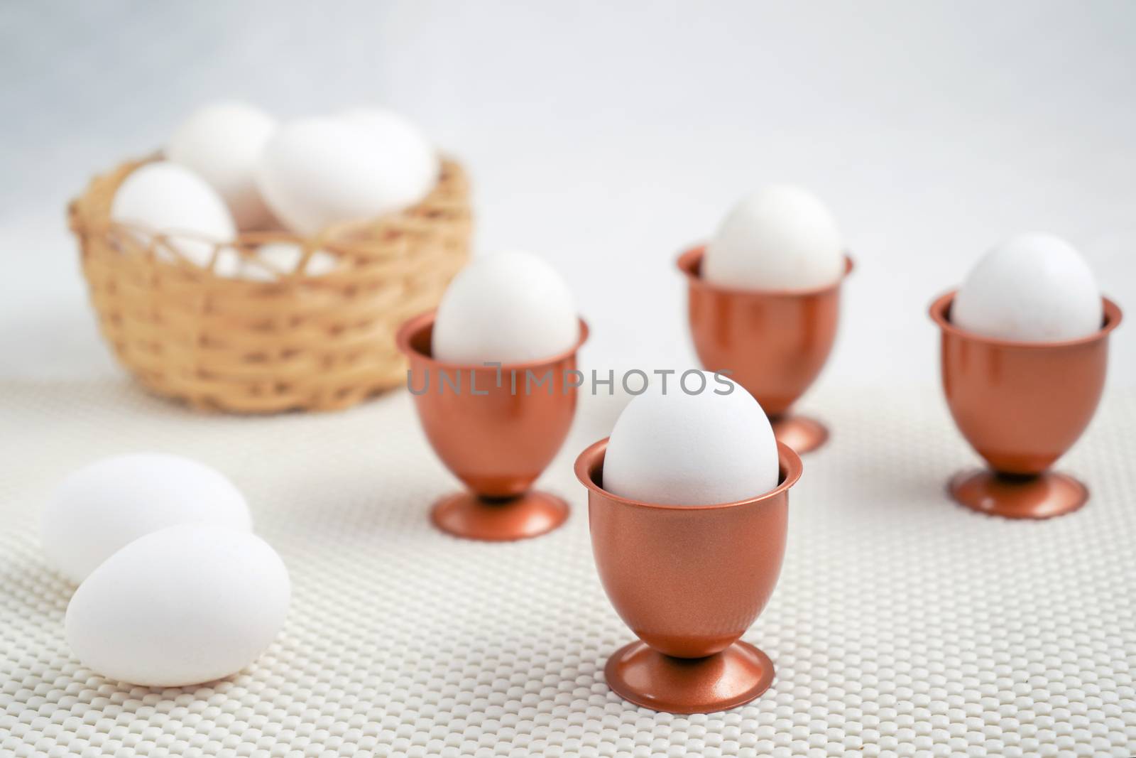 An eggs into a cooper eggs cup and three more cooper eggs cup with one eggs each and a basket with eggs at bottom