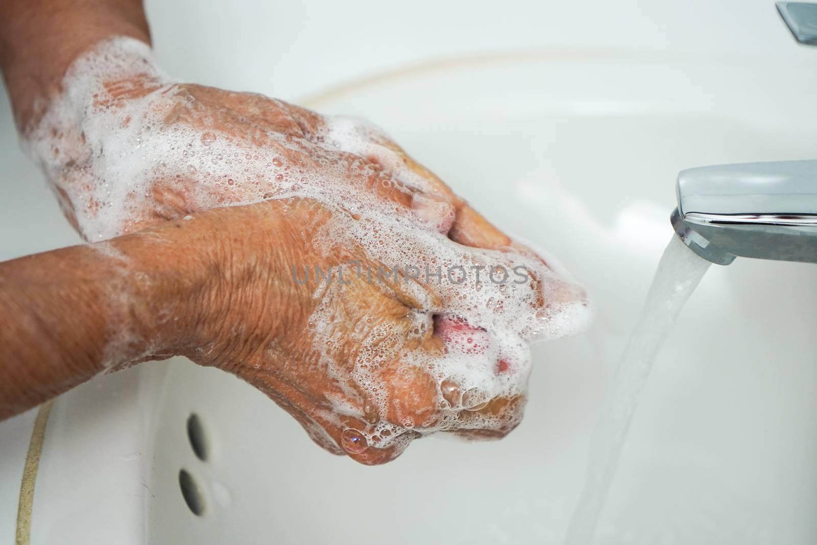 Pair of wrinkled hands washing in a sink