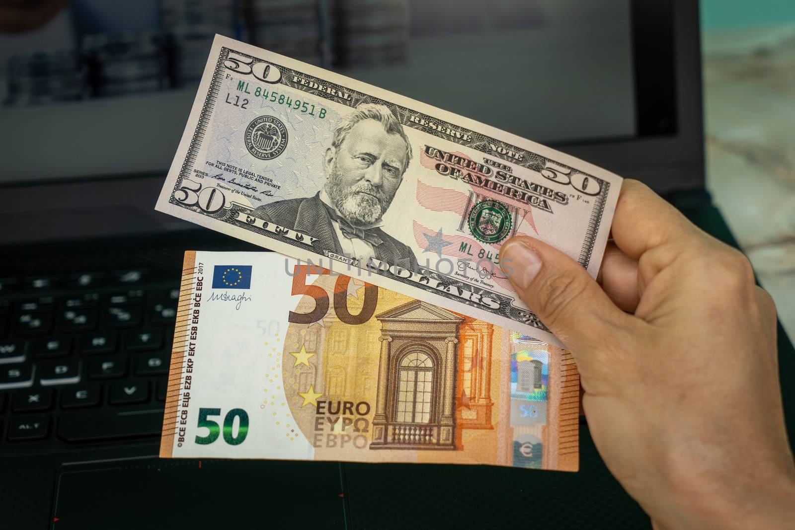 A hand holding two banknotes, one of fifty American dollars and the other of fifty euros