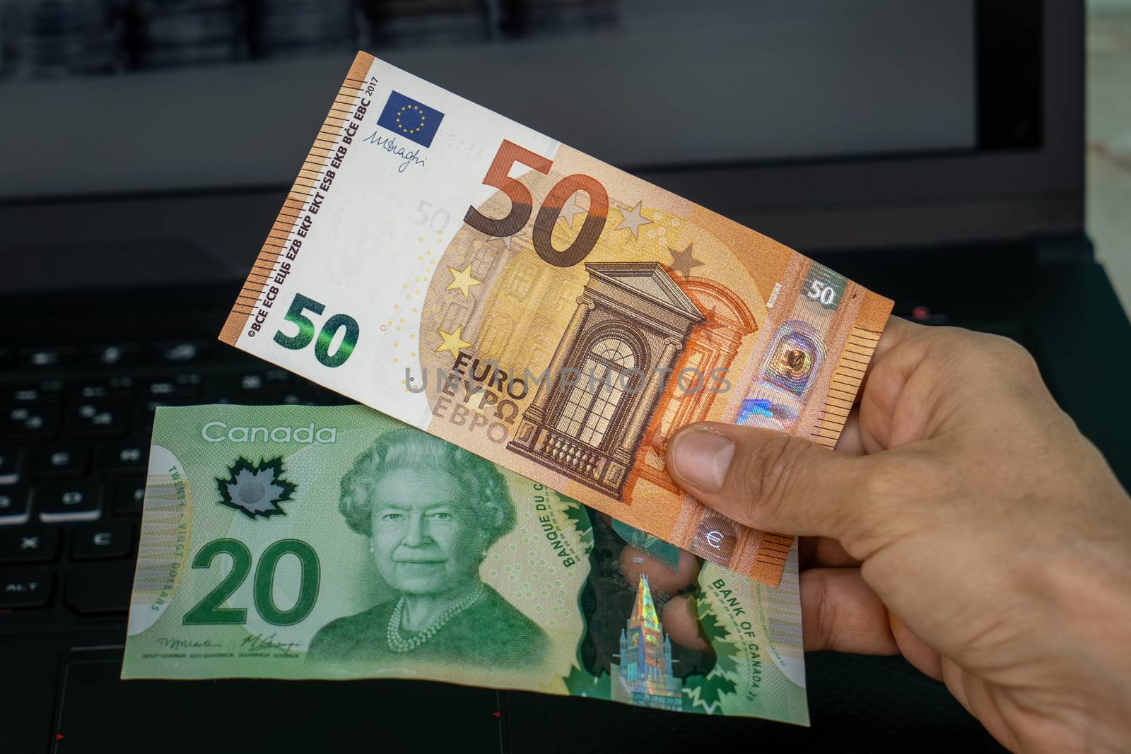 A hand holding two banknotes, one of twenty canadian dollars and the other of fifty euros