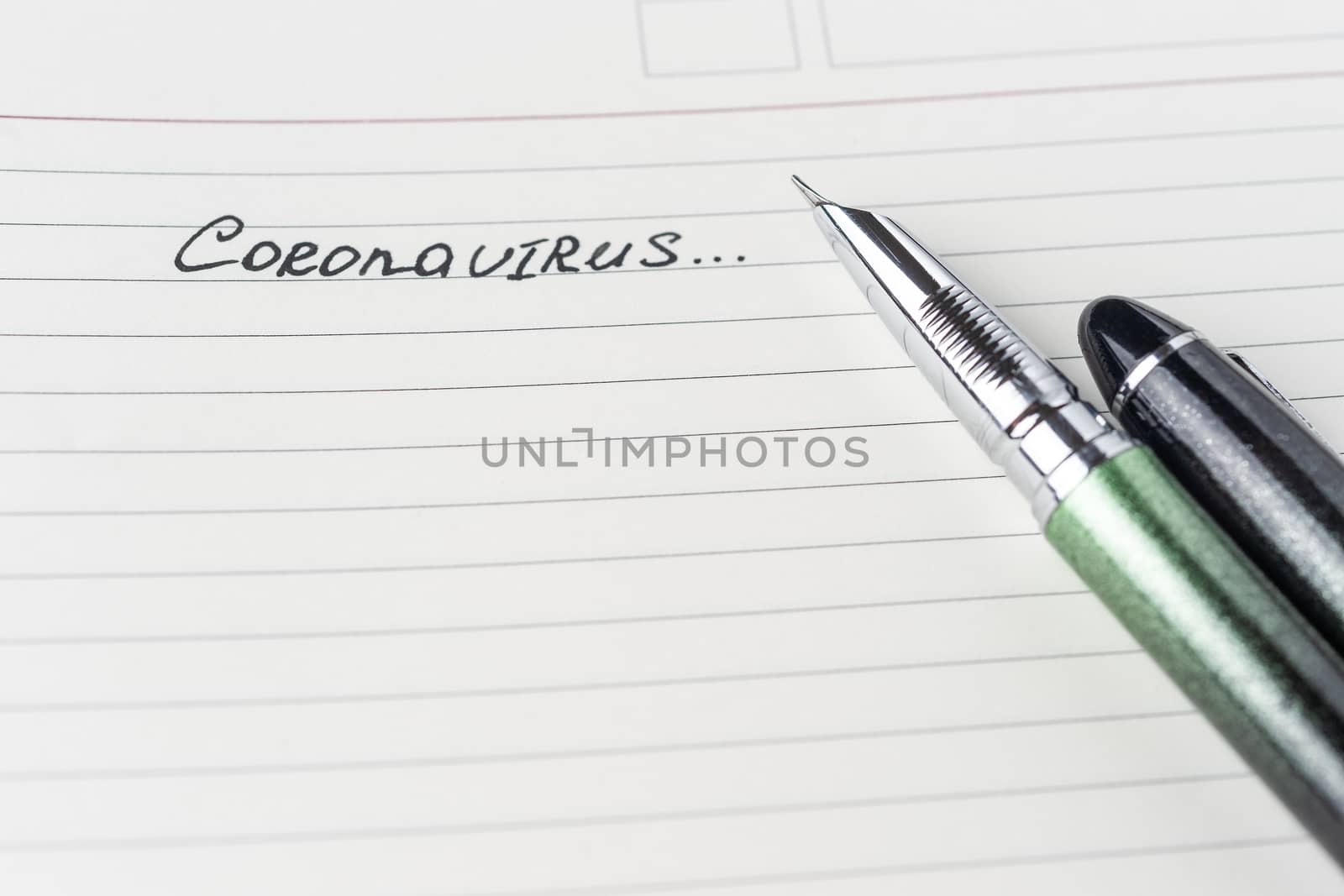 Coronavirus Covid-19 text hand-written on empty sheet in a daily planner. A part of planner on photo. Nearby lies luxury green fountain  pen. Sheet with copyspace. Top view.