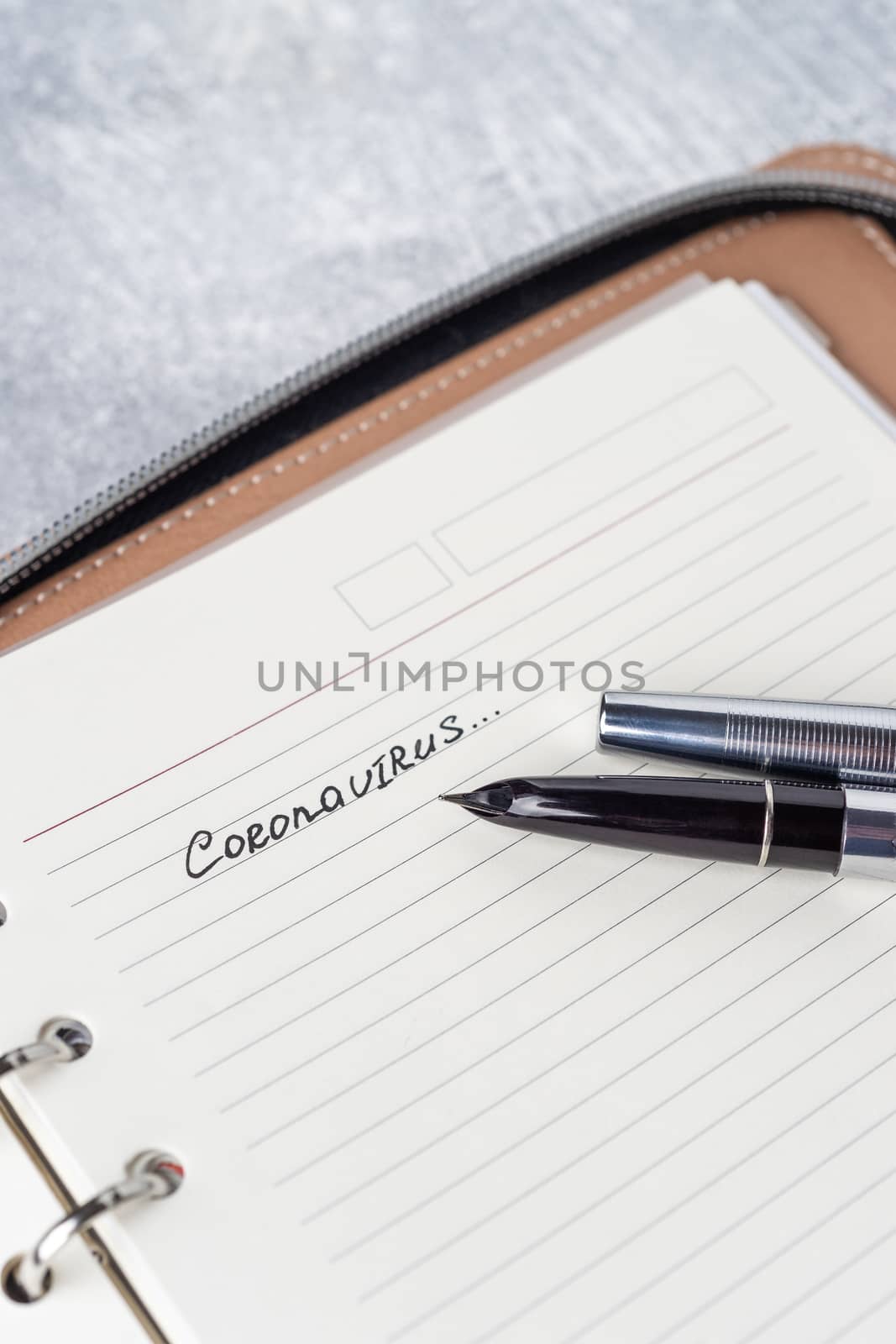 Coronavirus Covid-19 text hand-written on empty sheet in a daily planner. A part of planner on photo. Nearby lies luxury fountain  pen. Sheet with copyspace. Top view.
