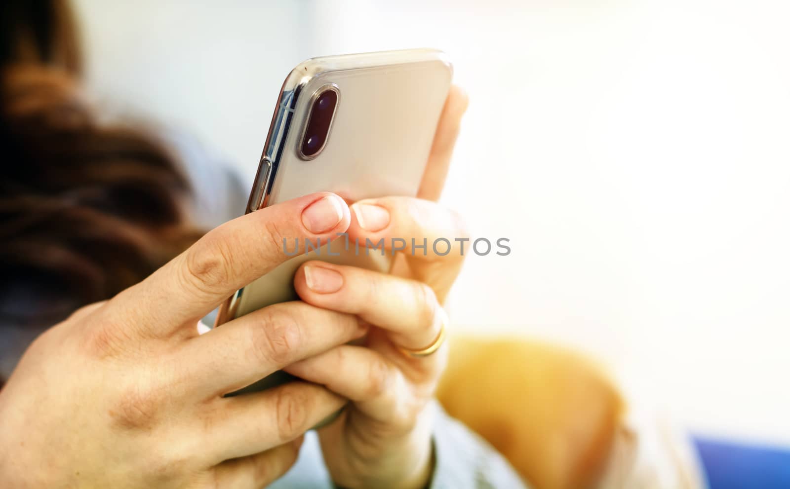 the hands of a young caucasian brunette woman while holding a smartphone typing on the touch screen. Technology and mobile connection.