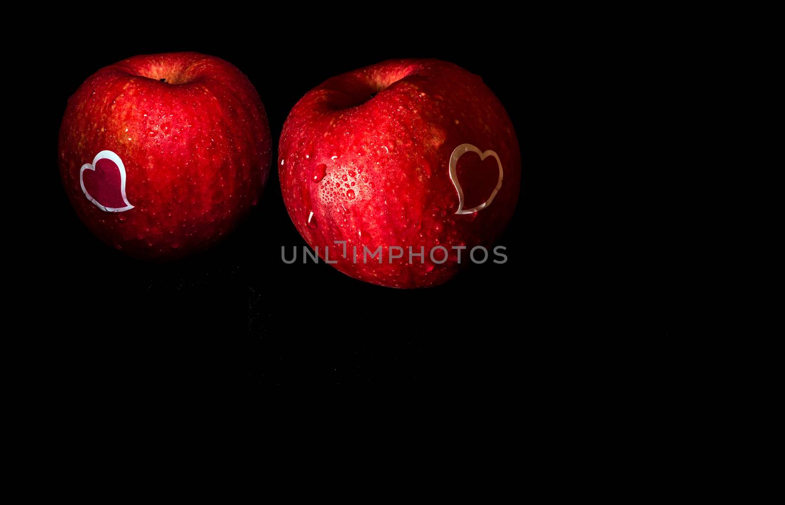 Heart shape sticker and water droplet on glossy surface of freshness red apple on black background