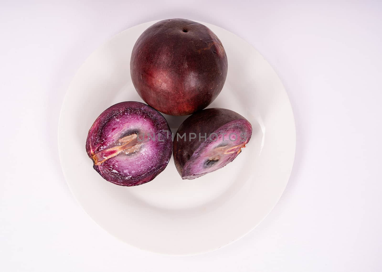 Two caimito fruit on a plate, one of them cut in two