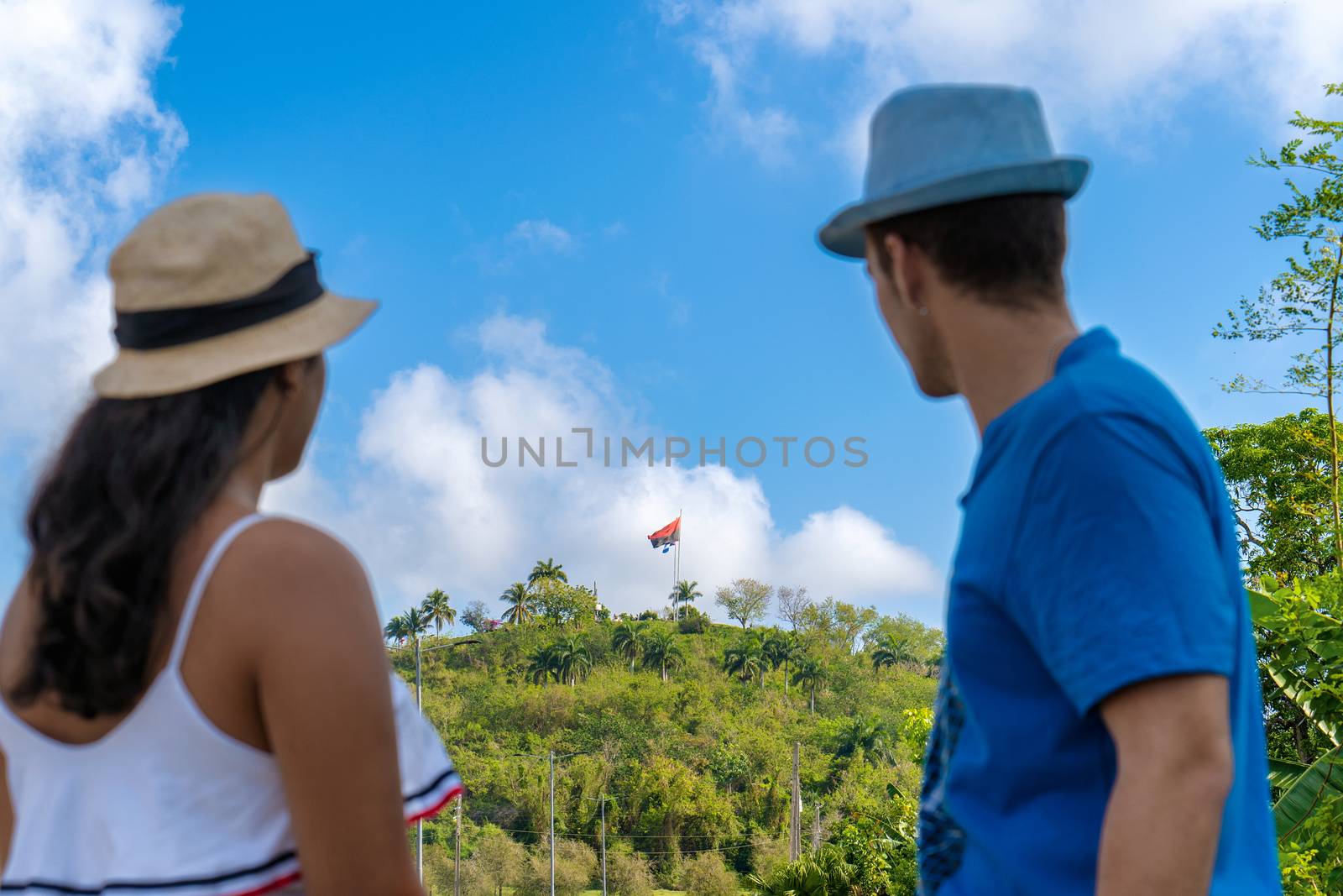 Young couple wearing hat in an unfocused closeup looking towards a hill covered with vegetation and two flags on top