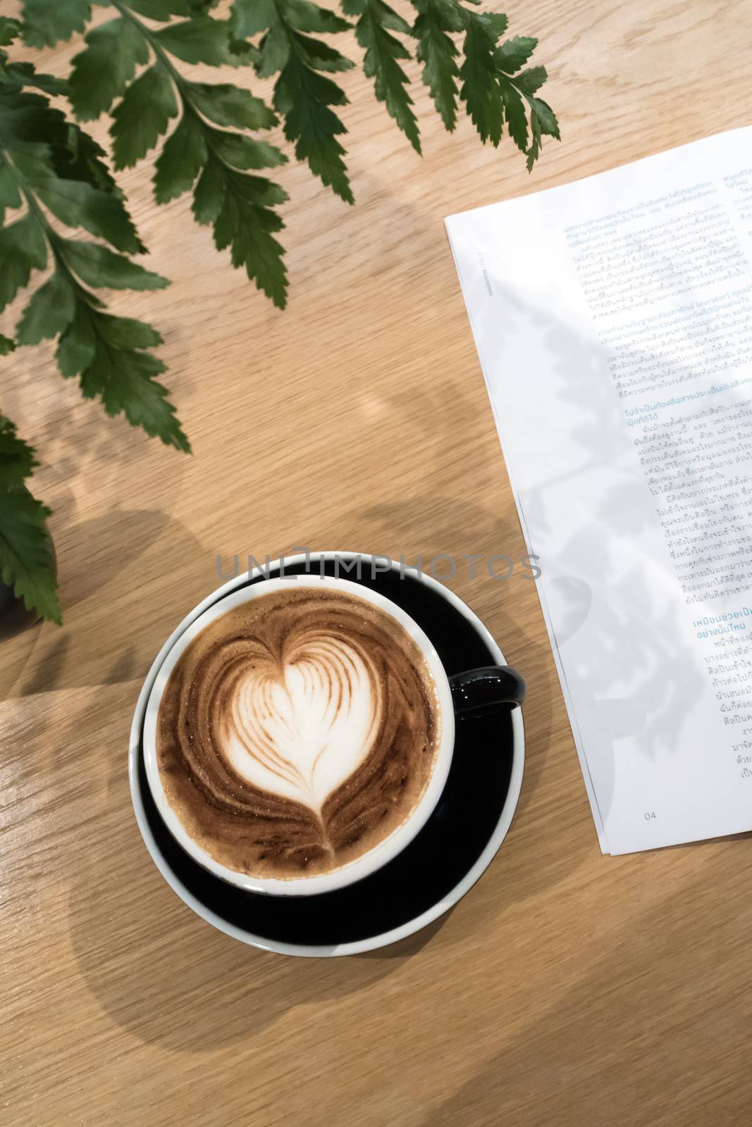 Coffee cup and a part of book on wood table with ornament fern l by Satakorn