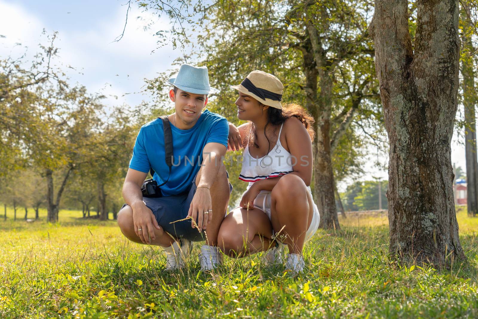 Couple of young people wearing hat crouching in a field with tamarind trees