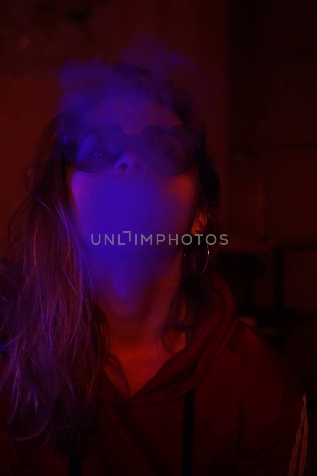 Close up vertical portrait of vaping girl in neon blue light