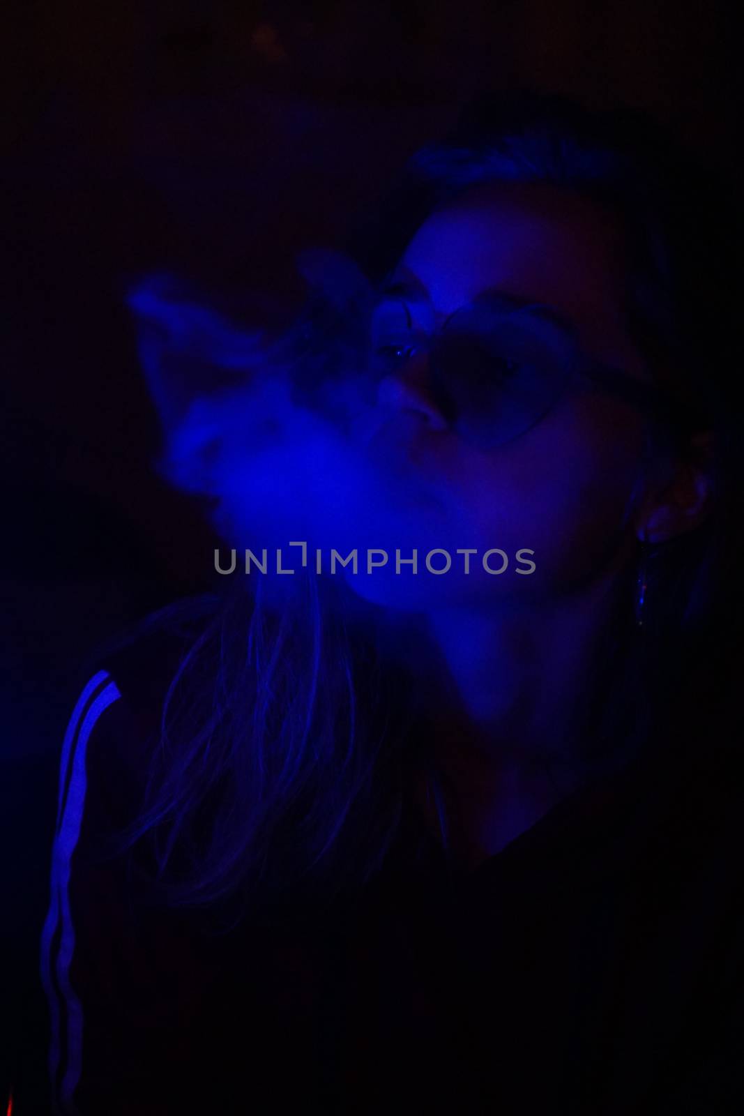 Close up vertical portrait of vaping girl in neon blue light