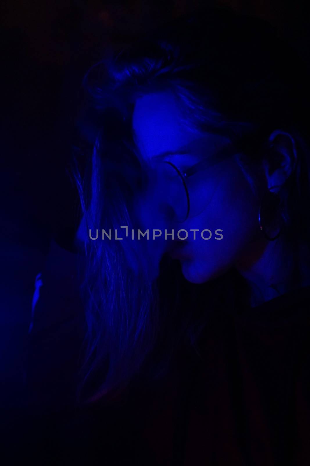 Close up vertical portrait of vaping girl in neon blue light