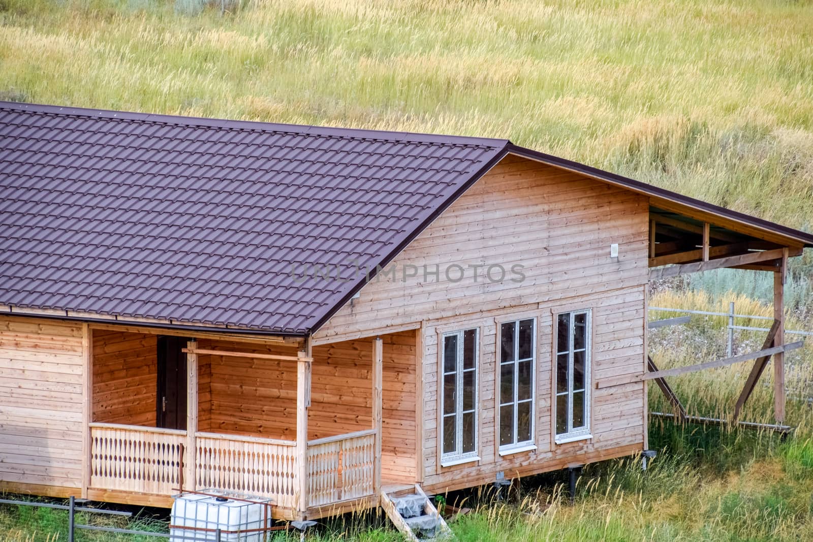A wooden house made of timber and planks with a roof made of metal. House among the steppe.