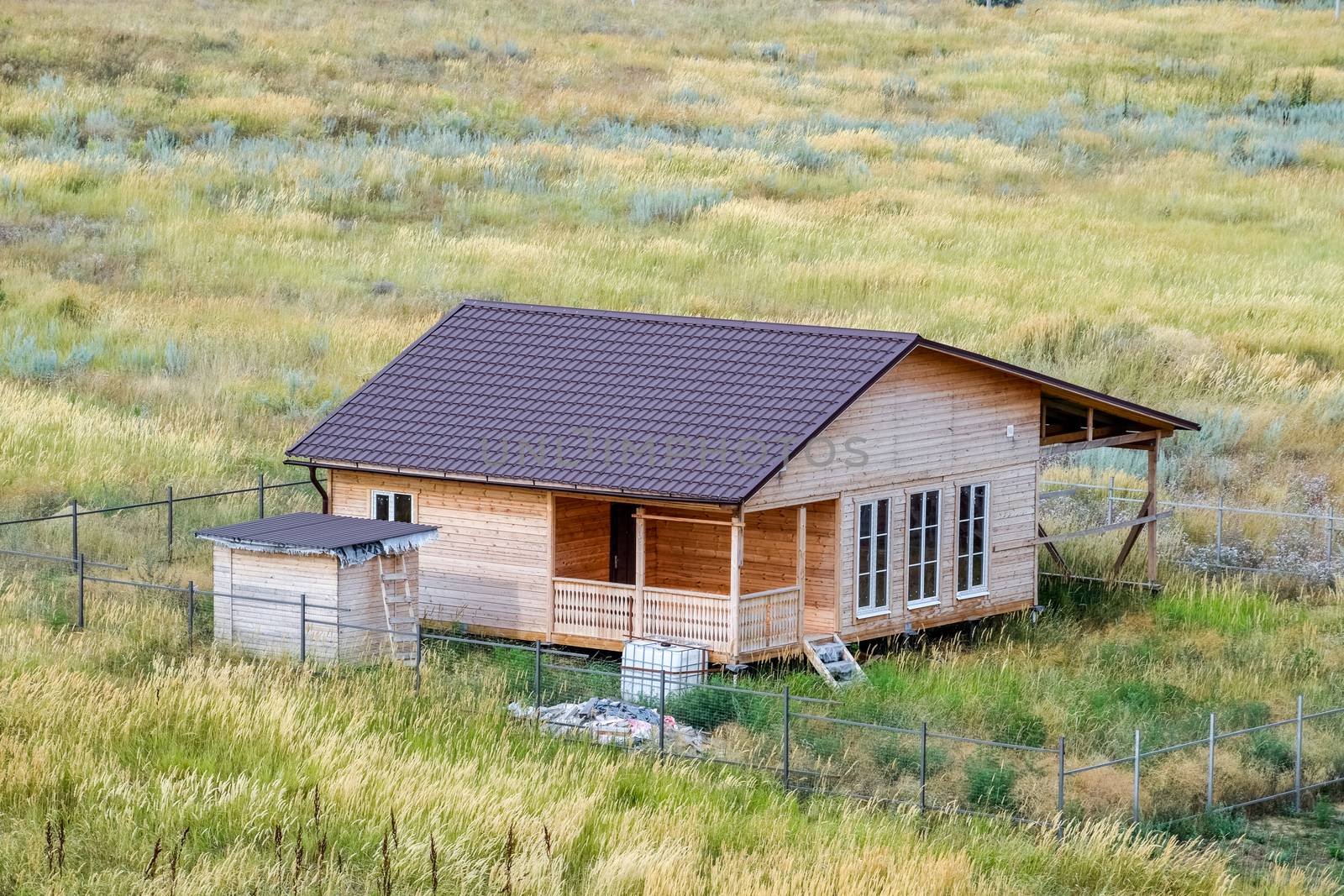 A wooden house made of timber and planks with a roof made of metal. House among the steppe.