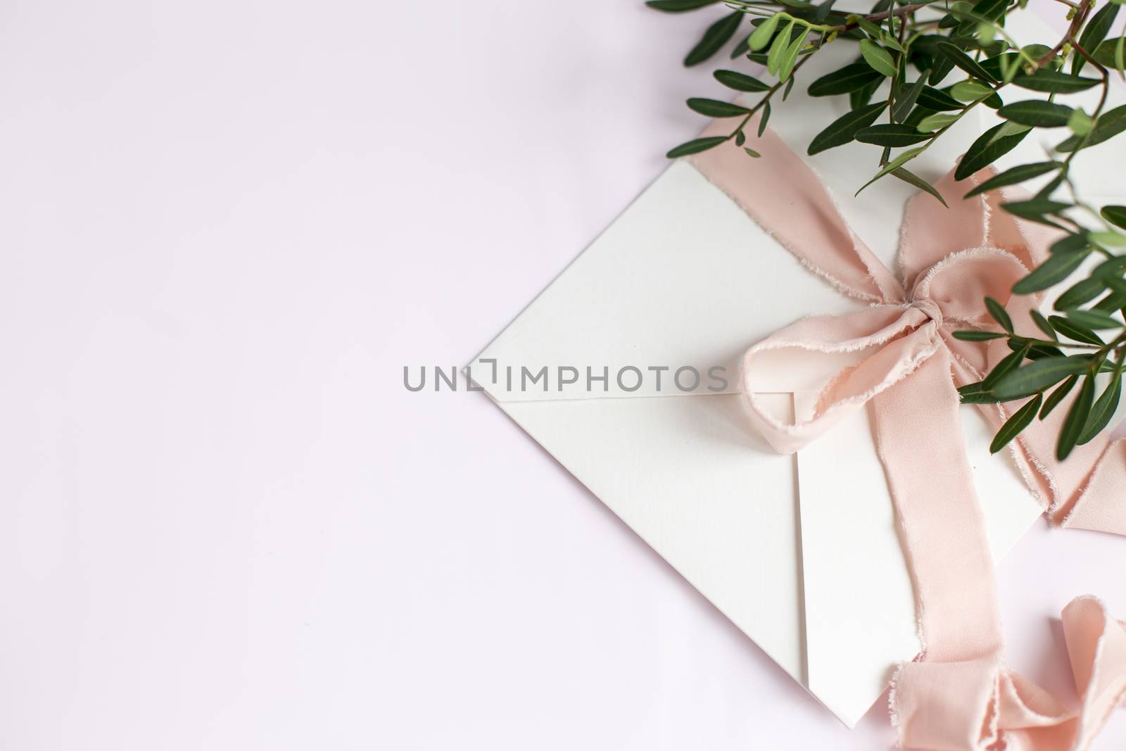 Envelope on a white-pink background with peach silk ribbon, green branch and flowers. Wedding invitation. Mother's day card. Place for text. Copy space.