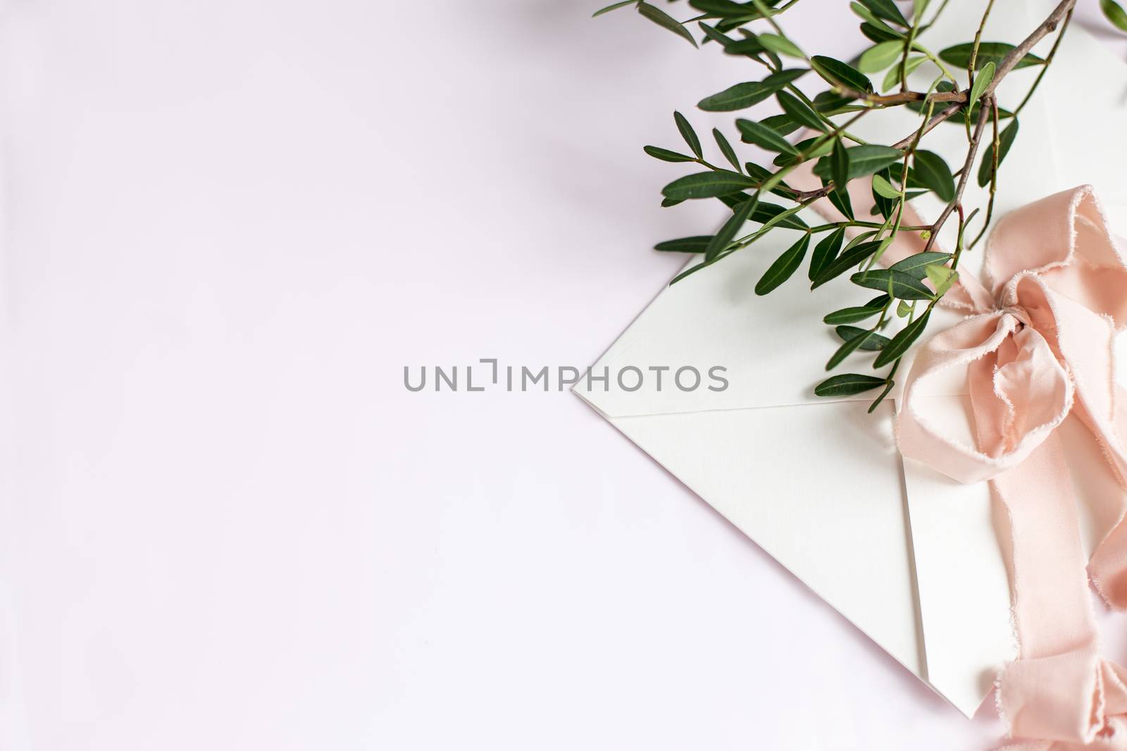 Envelope on a white-pink background with peach silk ribbon, green branch and flowers. Wedding invitation. Mother's day card. Place for text. Copy space.