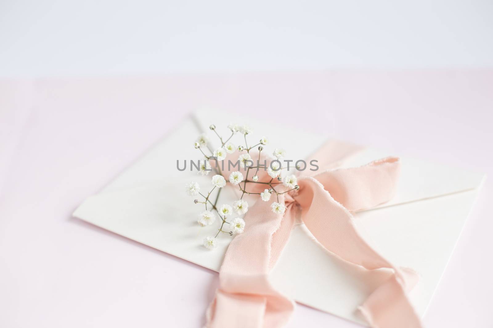 Envelope on a white-pink background with peach silk ribbon and pink flowers. Wedding invitation. Mother's day card. Place for text. Copy space.