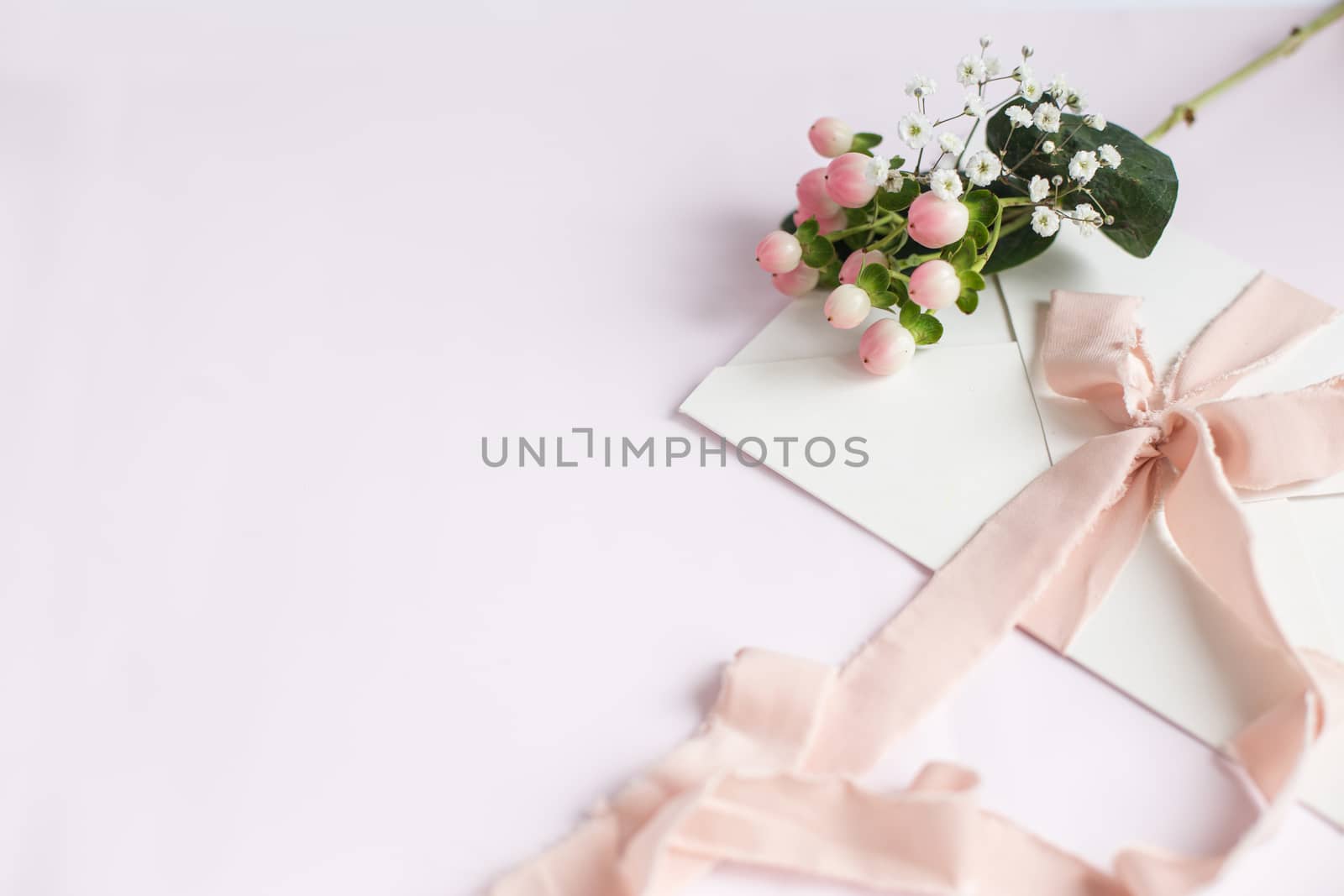 Envelope on a white-pink background with peach silk ribbon and pink flowers. Wedding invitation. Mother's day card. Place for text. Copy space.