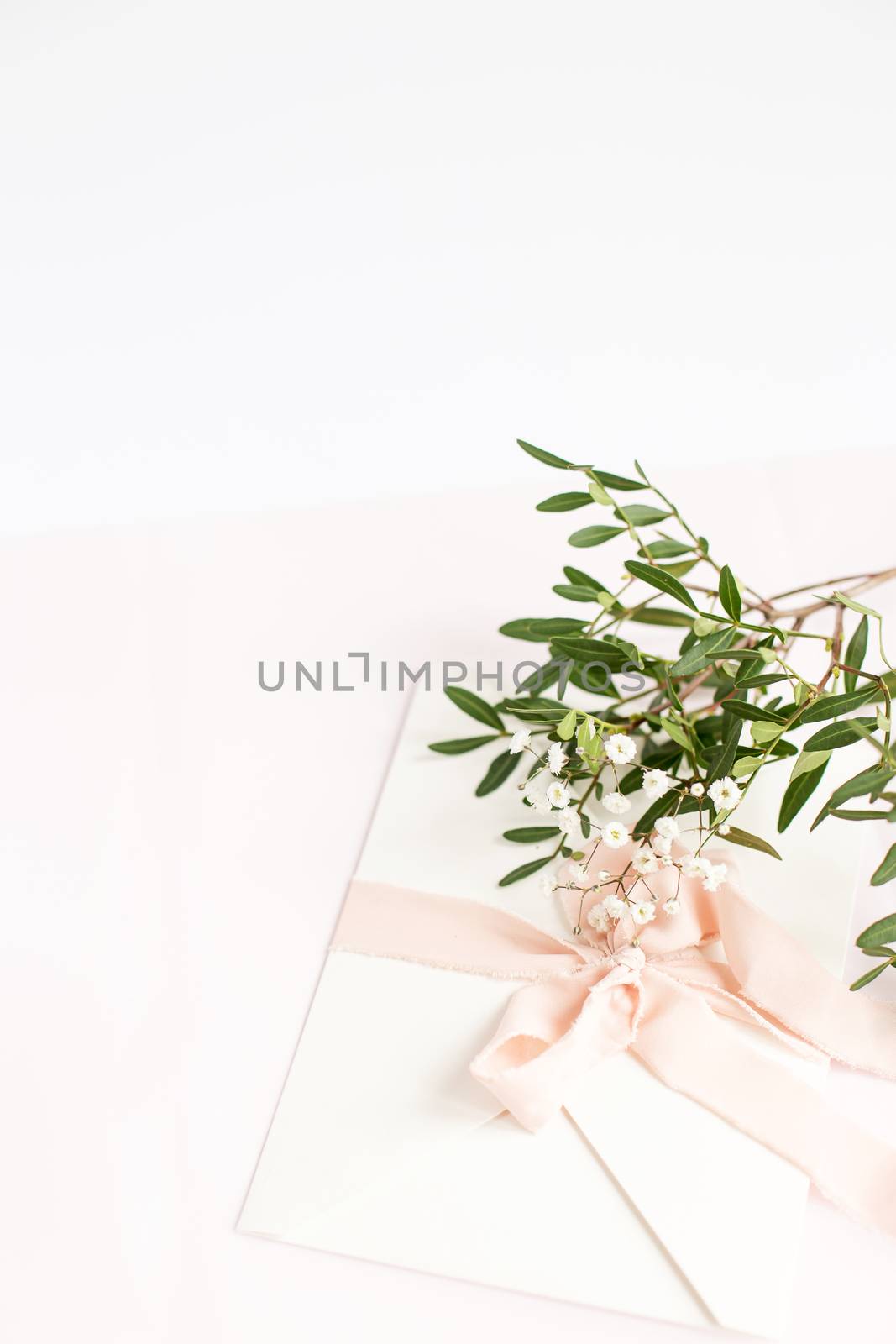 Envelope on a white-pink background with peach silk ribbon, green branch and flowers. Wedding invitation. Mother's day card. Place for text. Copy space.