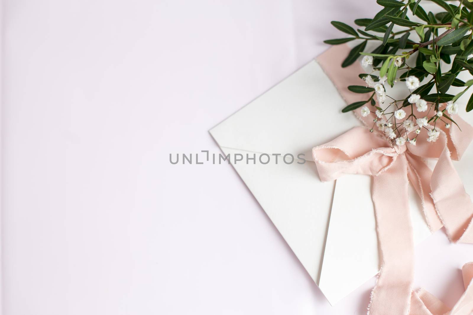 Envelope on a white-pink background with peach silk ribbon, green branch and flowers. Wedding invitation. Mother's day card. Place for text. Copy space.