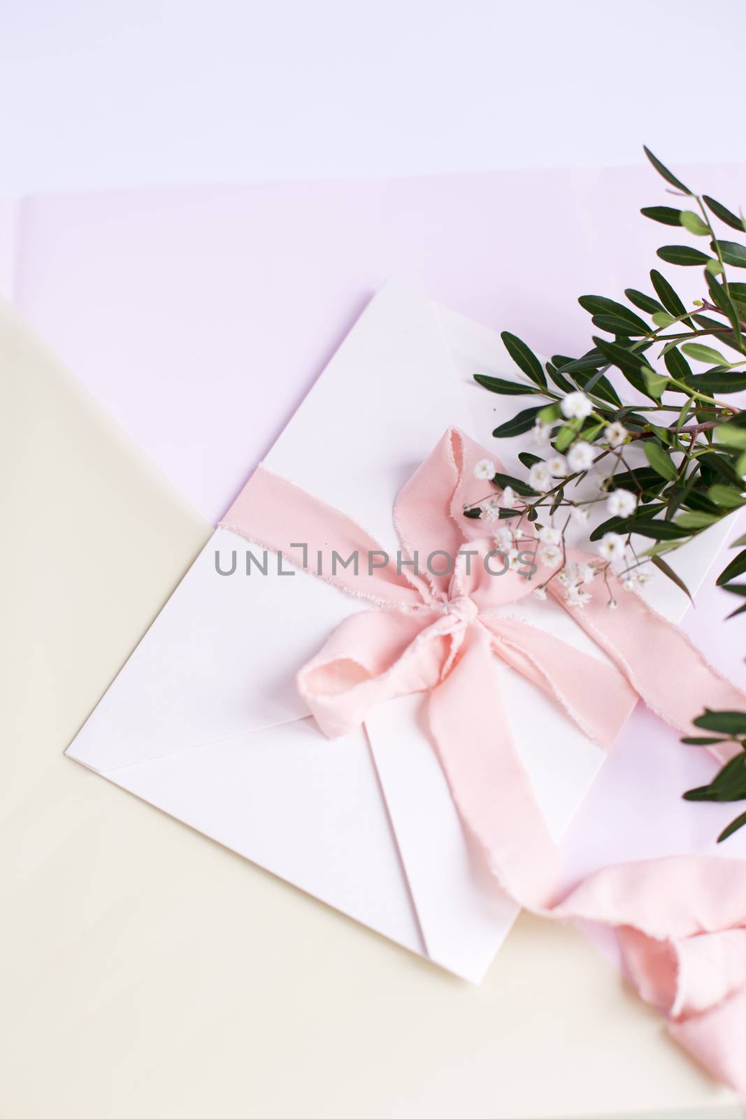 Envelope on a white-pink background with peach silk ribbon, green branch and flowers. Wedding invitation. Mother's day card. Place for text. Copy space.