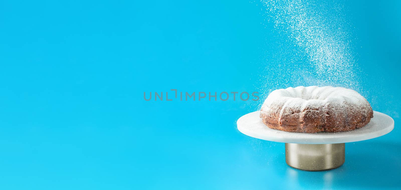 Icing sugar falling on bundt cake, blue background by fascinadora