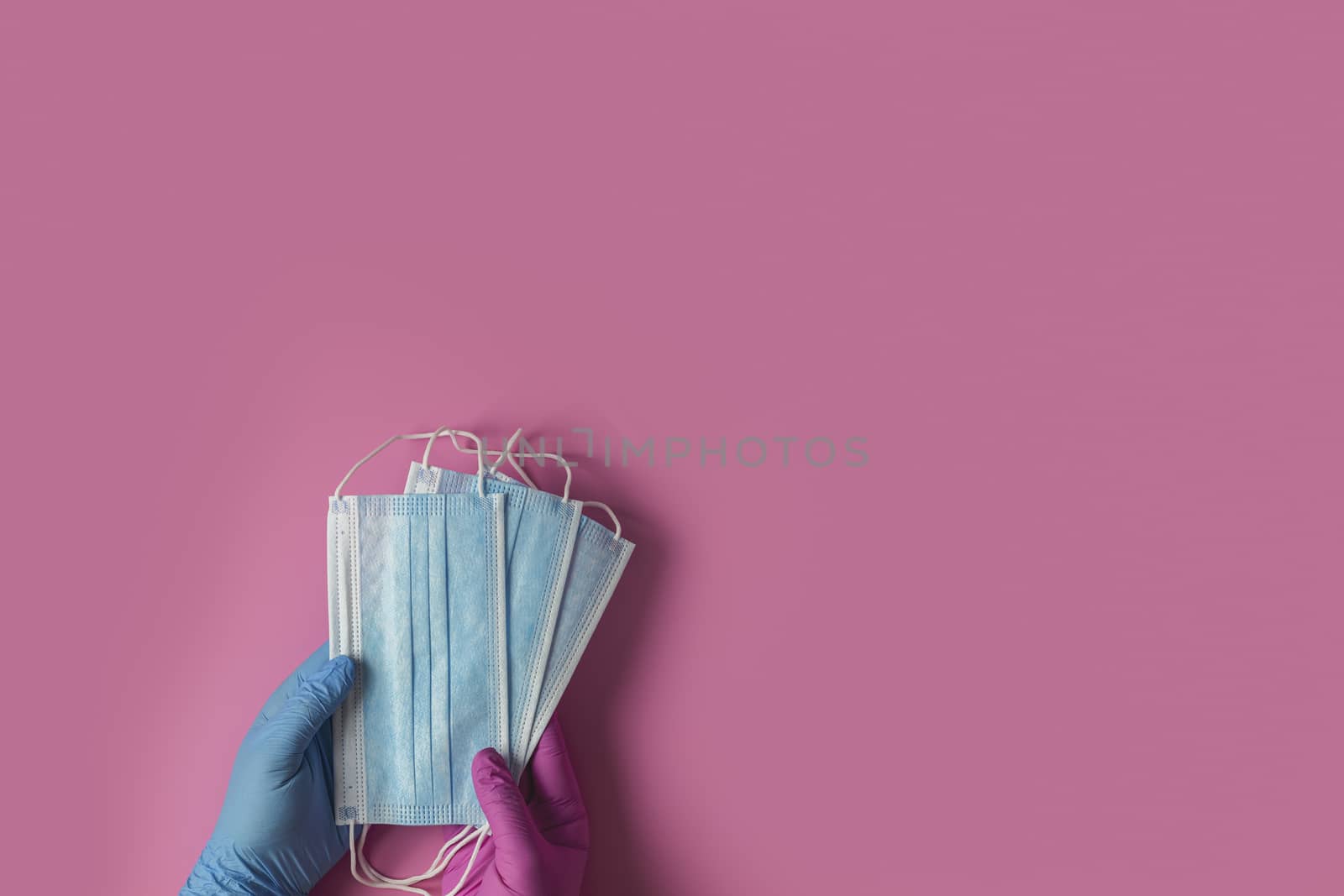 Doctor holds respiratory surgical face mask in hands blue and pink medical gloves on pink background. Pandemic corona virus, insurance, airborne diseases, SARS, grippe. 