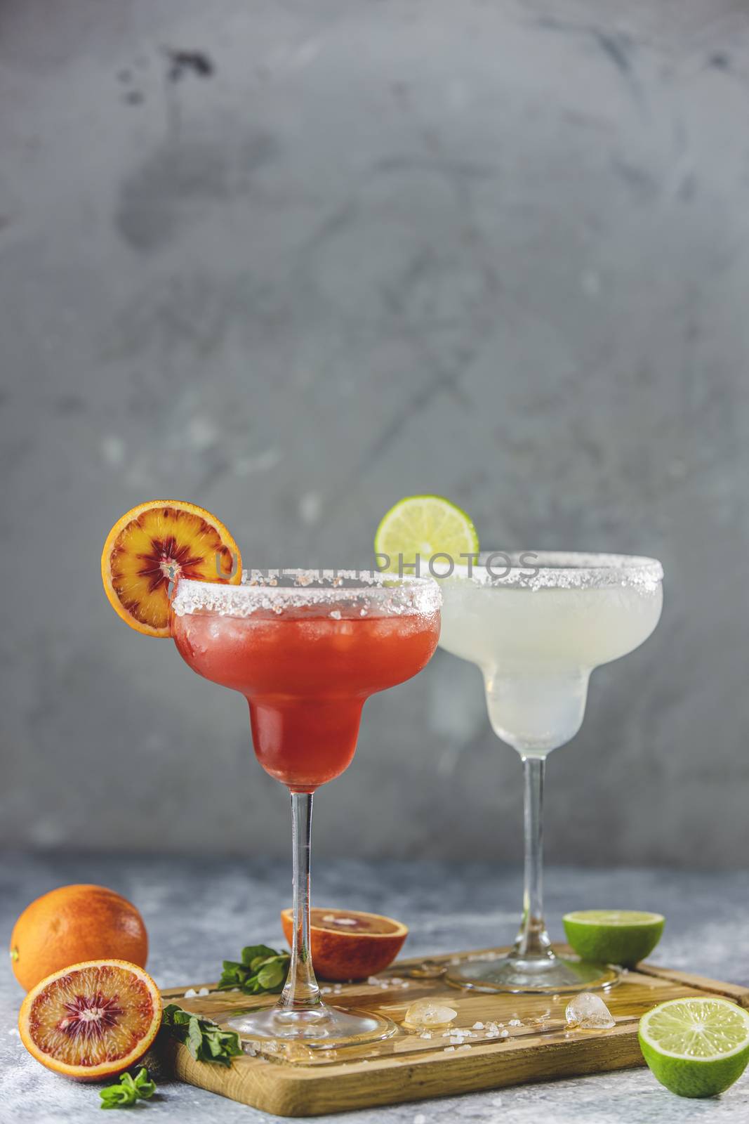 Frozen lime margarita and blood orange margarita cocktail mix in salt rimmed glasses garnished with slices of lime and orange. Focus on the citrus slice. Shallow depth of the field