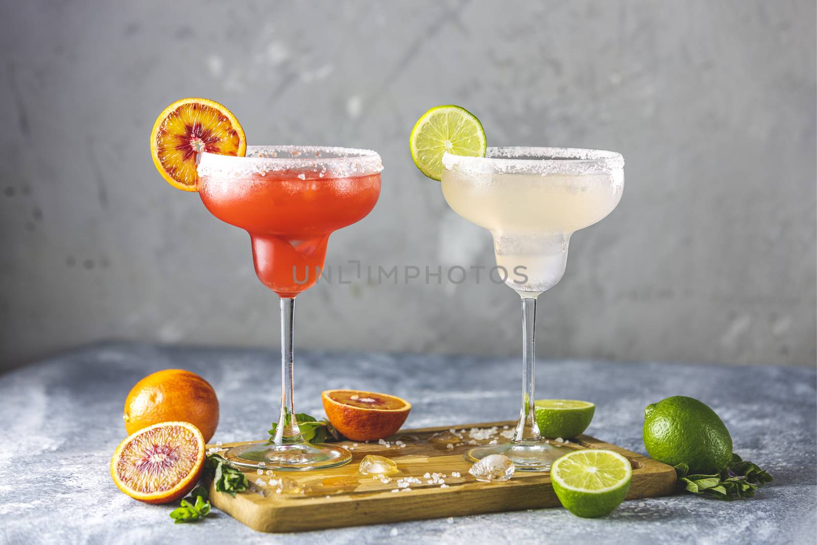 Frozen lime margarita and blood orange margarita cocktail mix in salt rimmed glasses garnished with slices of lime and orange. Focus on the citrus slice. Shallow depth of the field