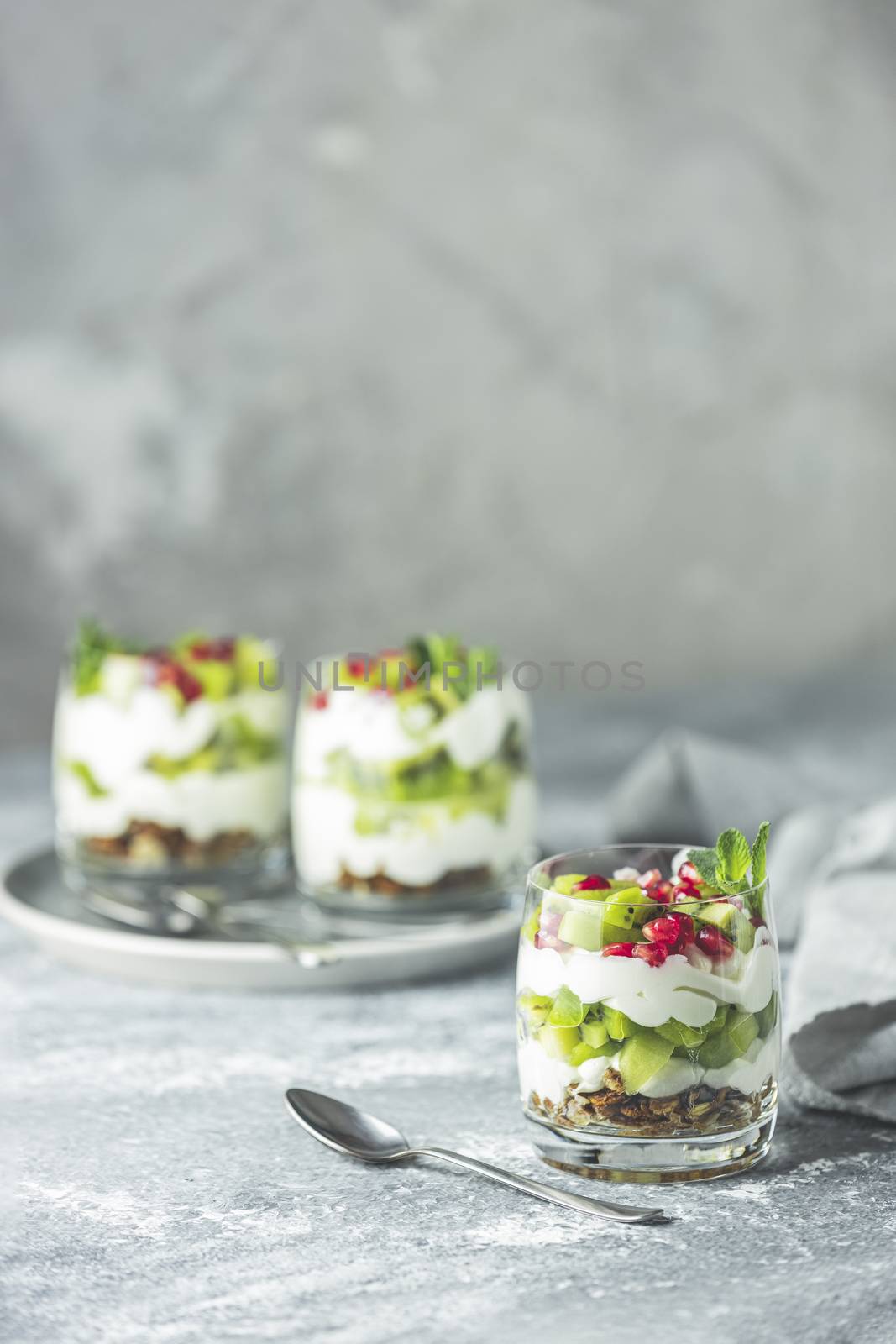 Kiwi parfait dessert in glass with ingredients. Yogurt, granola and fruits. Healthy snack or breakfast. Light gray concrete surface.