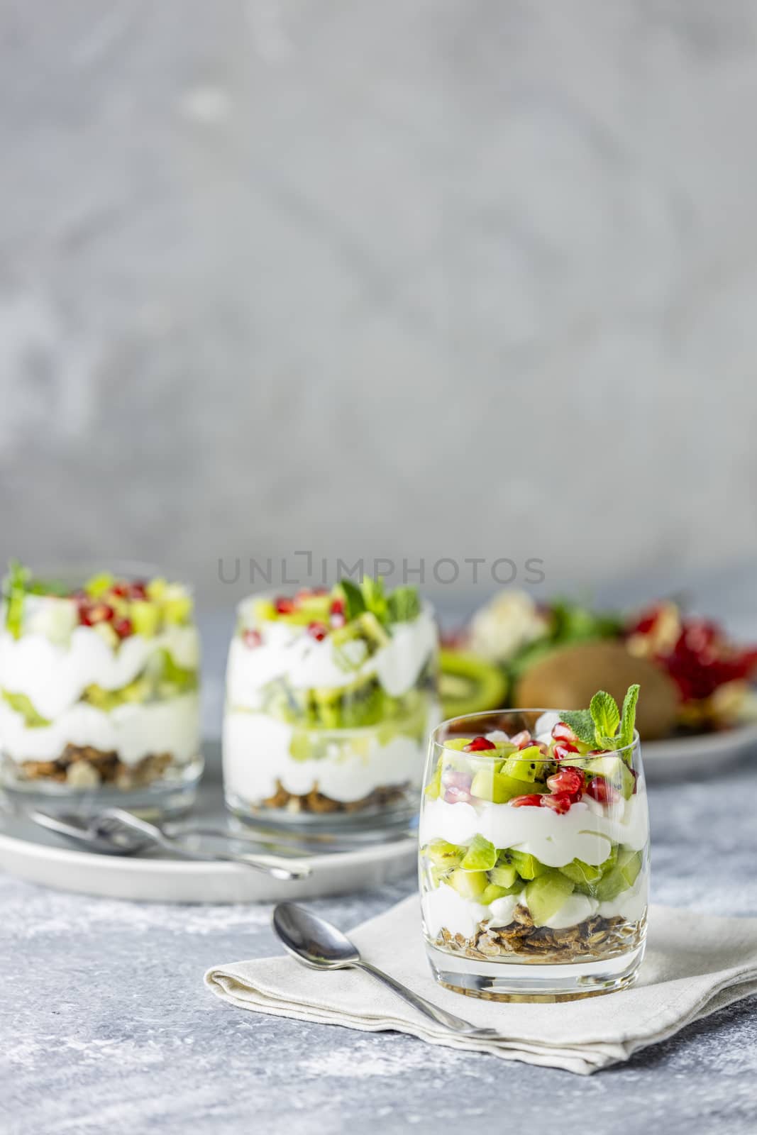 Homemade yogurt parfait with granola, kiwi fruit, pomegranate and mint in a glass for healthy breakfast on concrete background