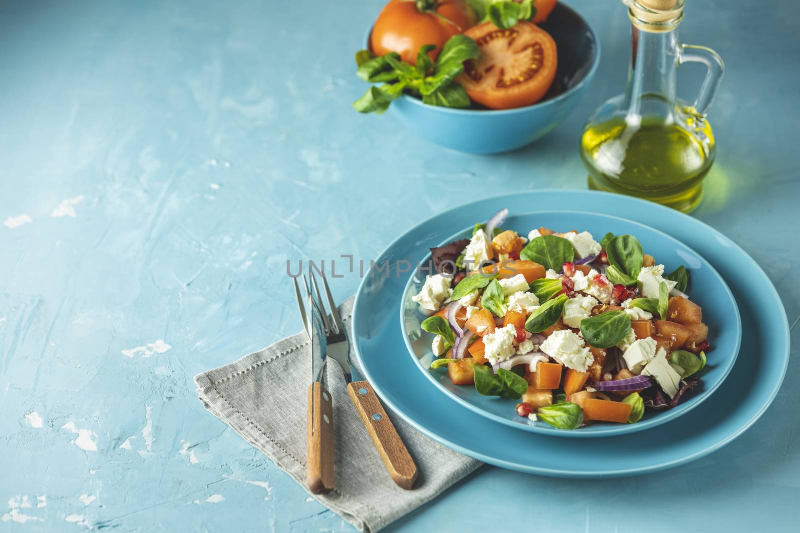 Blue plate of fresh superfoods healthy salad with red onion, tomatoes, doucette (lambs lettuce, corn salad, field salad) and feta cheese. Light blue surface	