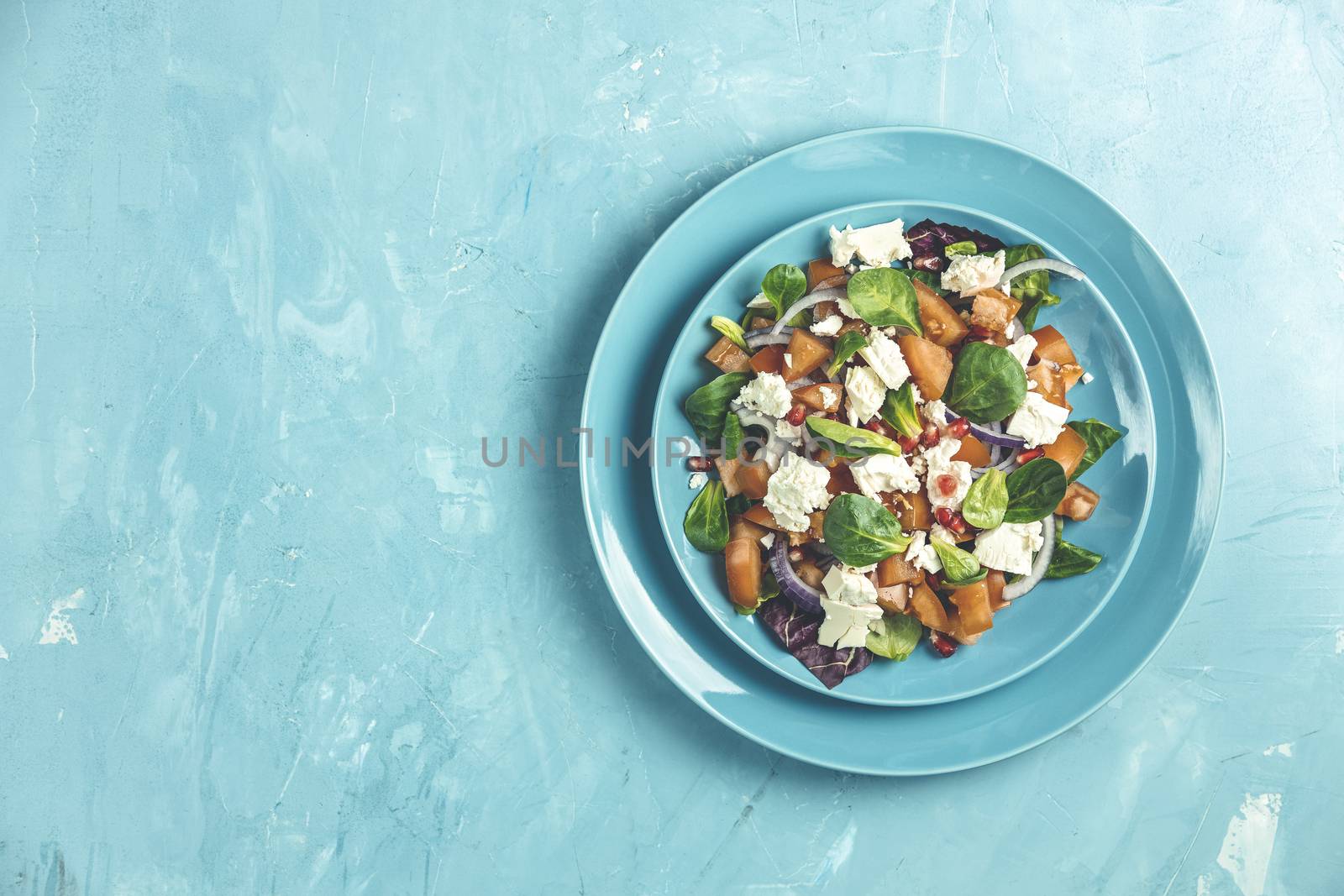 Blue plate of fresh superfoods healthy salad with red onion, tomatoes, doucette (lambs lettuce, corn salad, field salad) and feta cheese. Light blue surface, top view, flat lay, copy space.