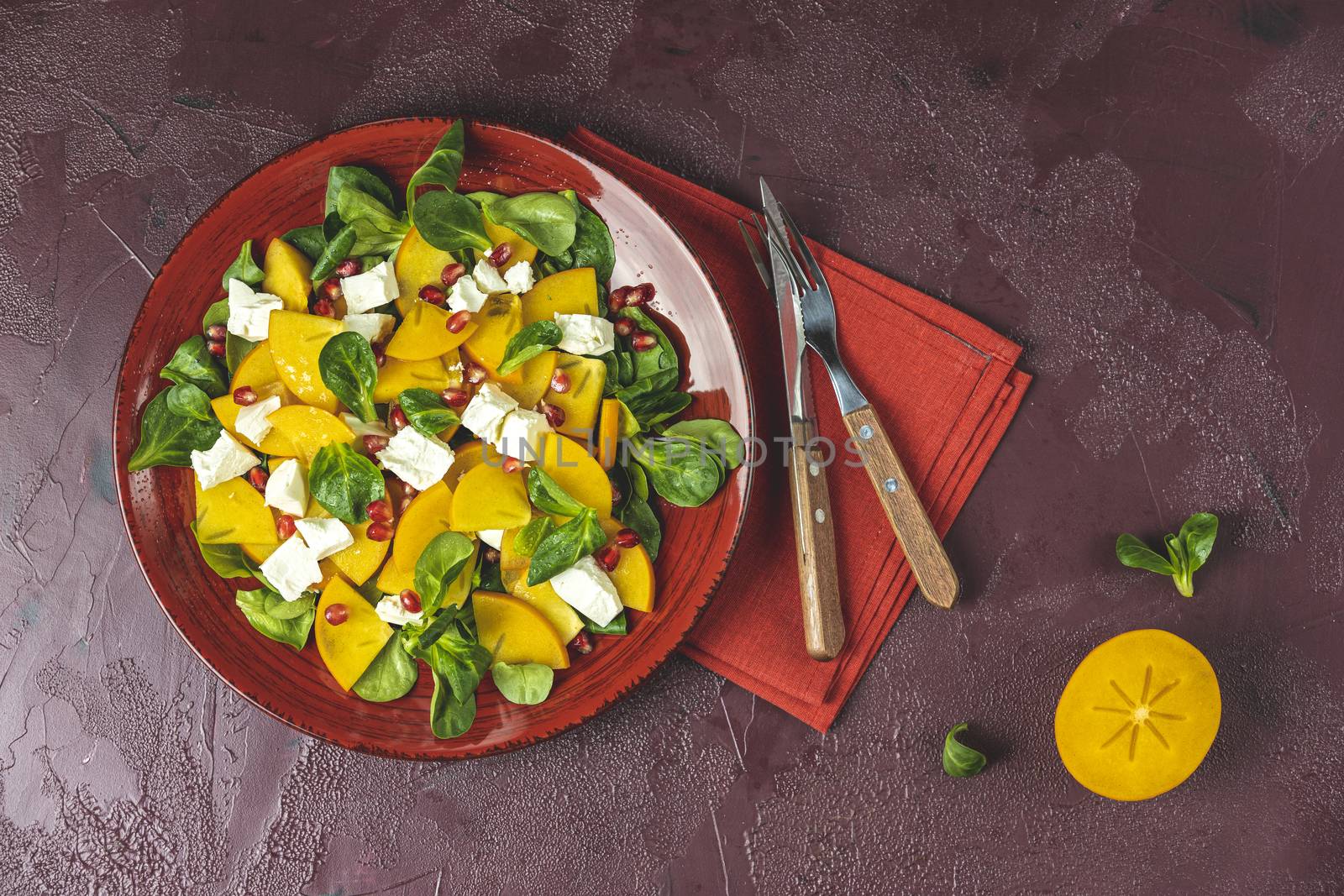 Healthy salad with persimmon, doucette (lambs-lettuce, cornsalad, feld salad) and feta cheese. Fitness food, superfoods vitamin persimmon salad. Top view, flat lay, copy space.