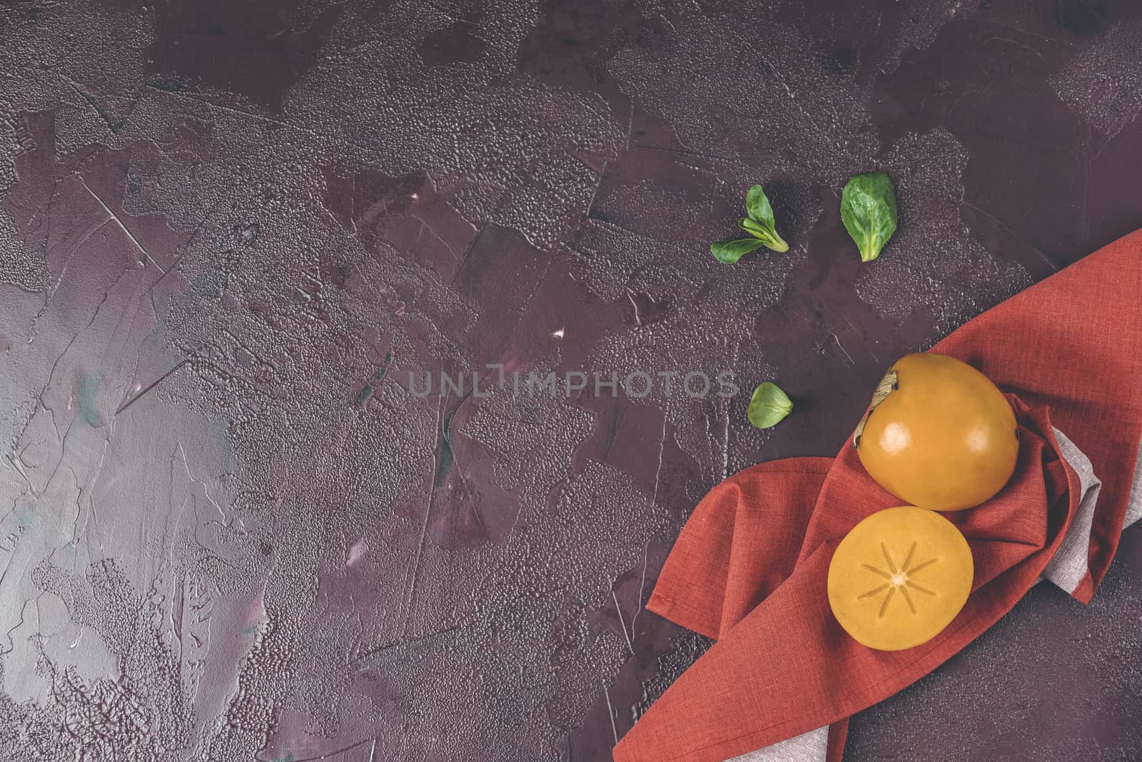 Healthy food background with persimmon and doucette (lambs-lettuce, cornsalad, field salad) with napkin on a red background, top view flat lay.