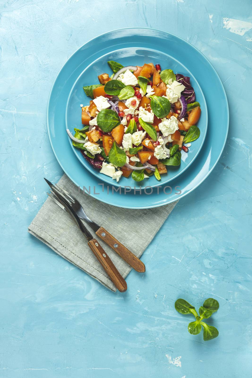 Blue plate of fresh superfoods healthy salad with red onion, tomatoes, doucette (lambs lettuce, corn salad, field salad) and feta cheese. Light blue surface, cutlery, top view, flat lay, copy space.