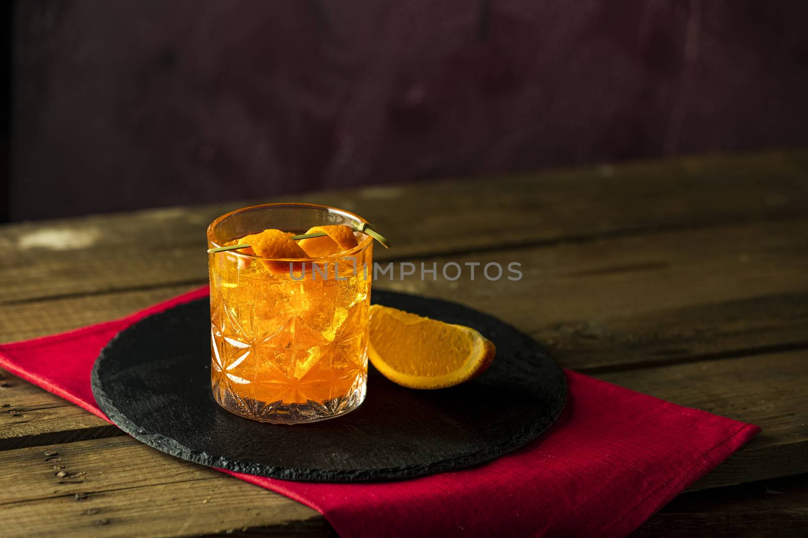 Glass of the cocktail negroni on a old wooden board. Drink with gin, campari martini rosso and orange, an italian cocktail, an aperitif, first mixed in Firenze Italy in 1919 alcoholic bitter cocktail