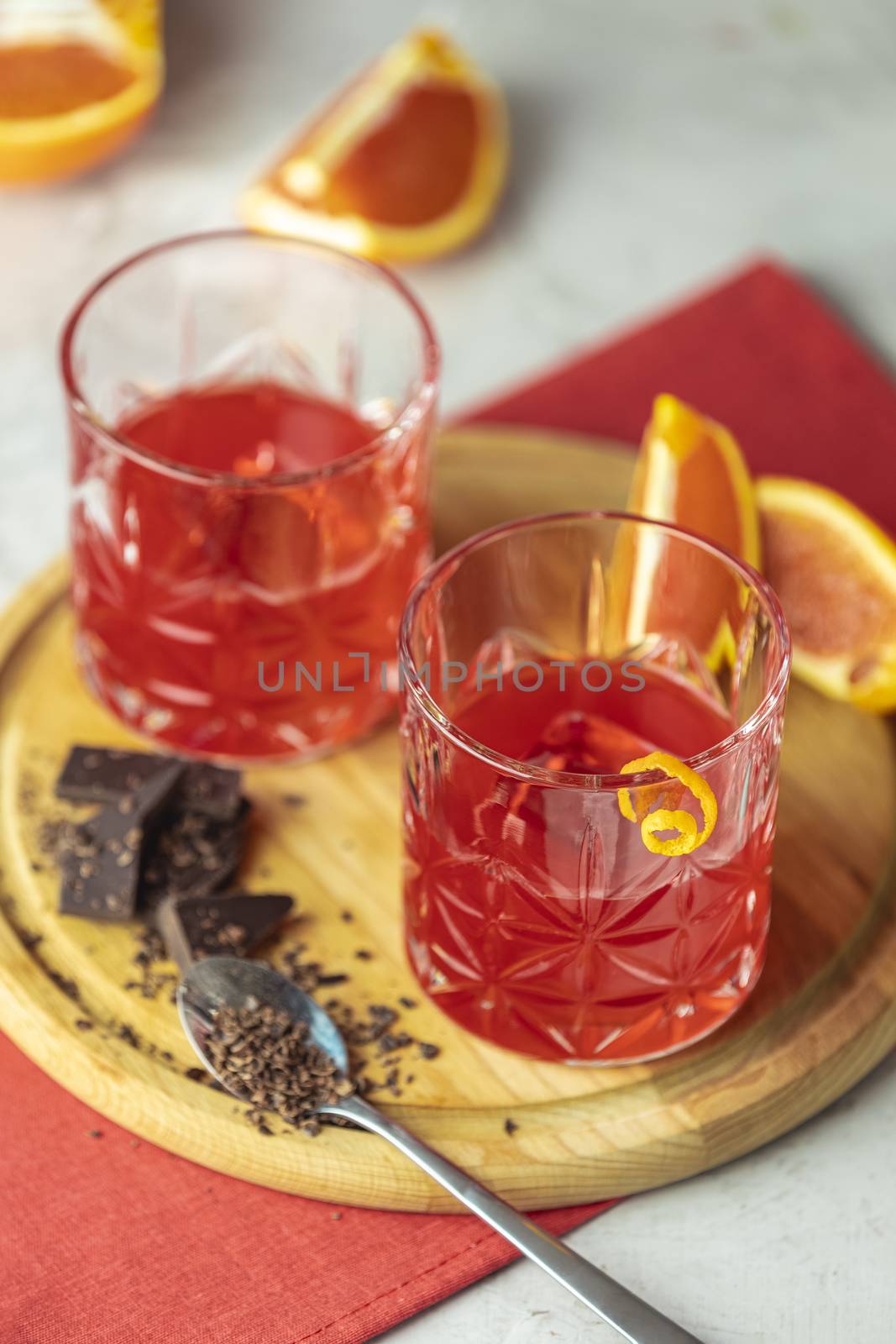 Two glasses of chocolate red orange negroni, an italian cocktail, an aperitif, first mixed in Firenze, Italy, in 1919, alcoholic bitter cocktail served by ingredients on the light gray table.