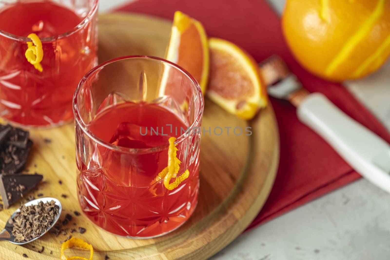 Two glasses of chocolate red orange negroni, an italian cocktail, an aperitif, first mixed in Firenze, Italy, in 1919, alcoholic bitter cocktail served by ingredients on the light gray table.