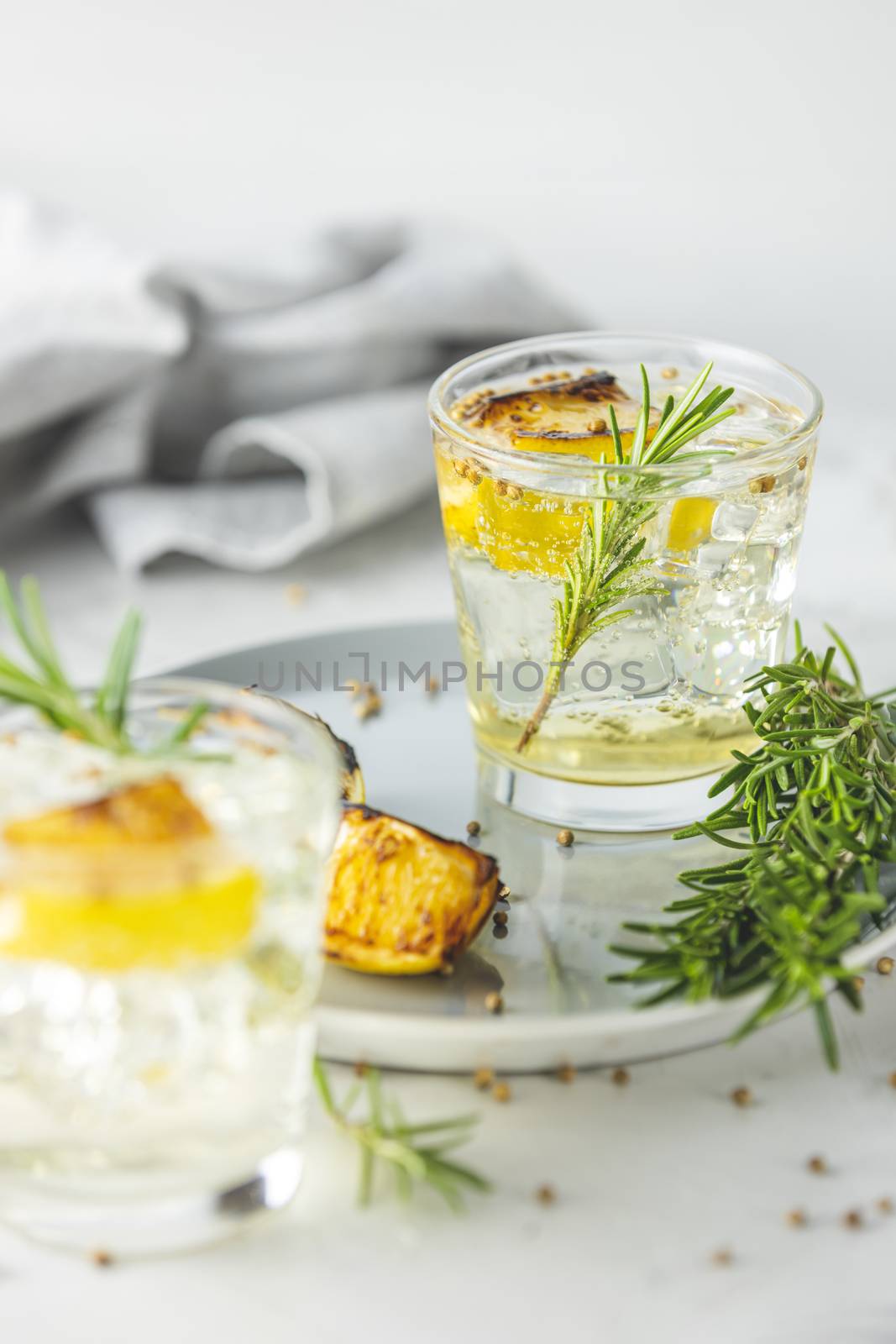 Glasses of Gin and Tonic with Charred Lemon, Rosemary and Coriander is a flavors are perfectly balanced refreshing cocktail. on light background, close up surrounded ingredients, selective focus