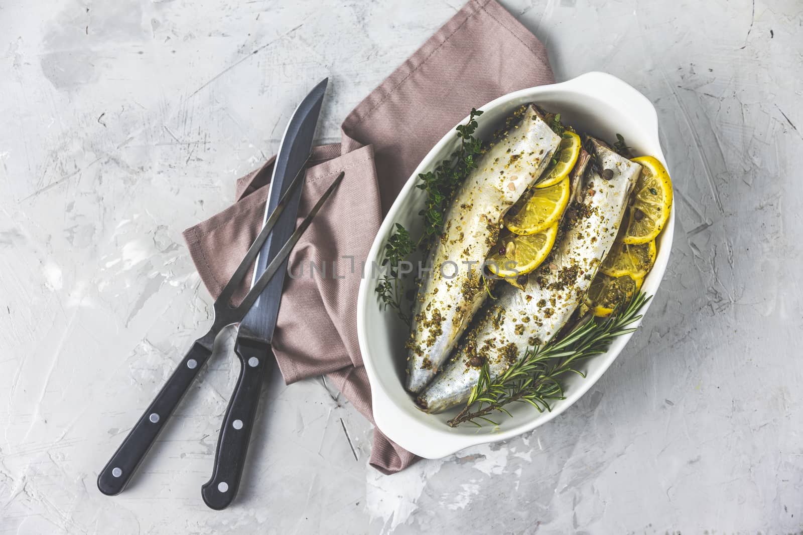 Mackerels served on white dish with lemon, thyme, rosemary and spices. Raw marinated fishes on light gray surface. Seafood background.