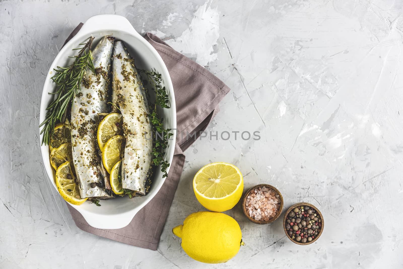 Mackerels served on white dish with lemon, thyme, rosemary and spices. Raw marinated fishes on light gray surface. Seafood background.