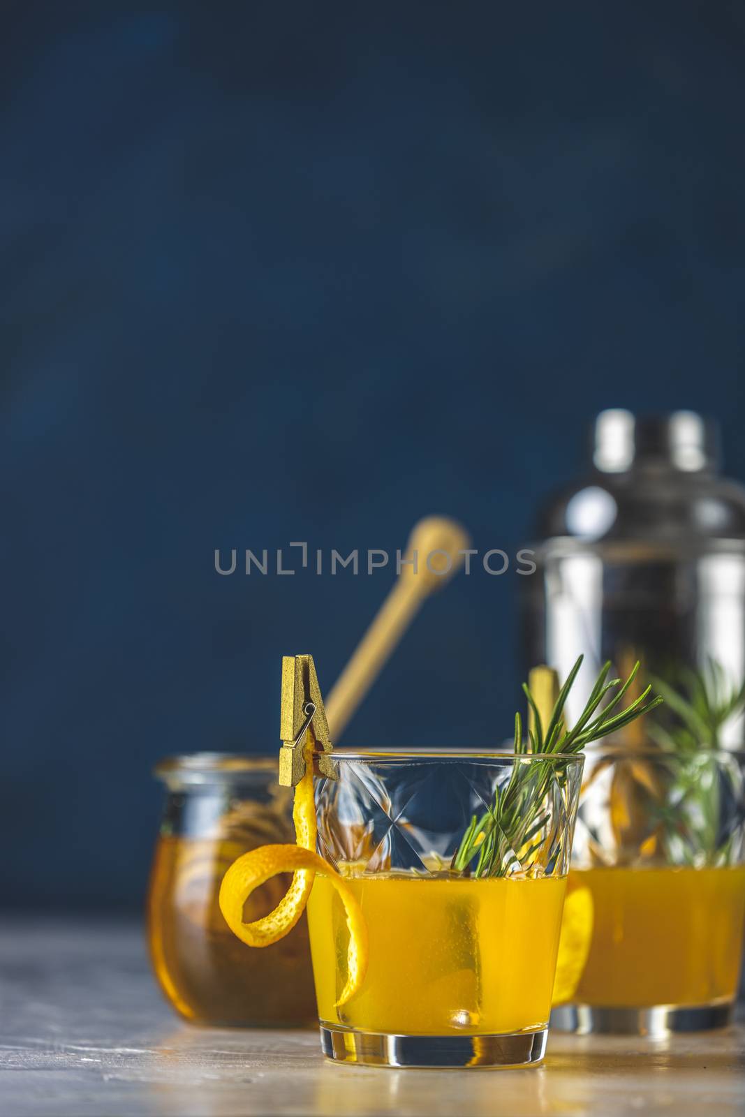 Two glasses of honey bourbon cocktail with rosemary simple syrup or homemade whiskey sour cocktail drink with orange and rosemary decoration orange peel, jar of honey  and bartender tools