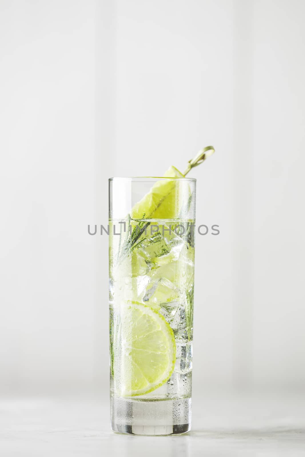 Refreshing lemon lime drink with ice cubes in glass goblets against a light gray background. Summer fresh lemon soda cocktail with rosemary, selective focus